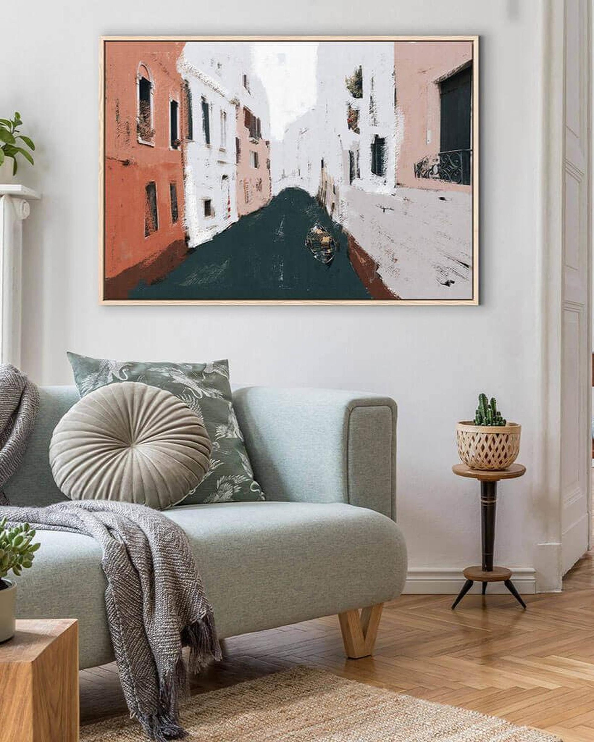Living room with a light blue sofa, decorative pillows, and a large framed painting of a canal scene.