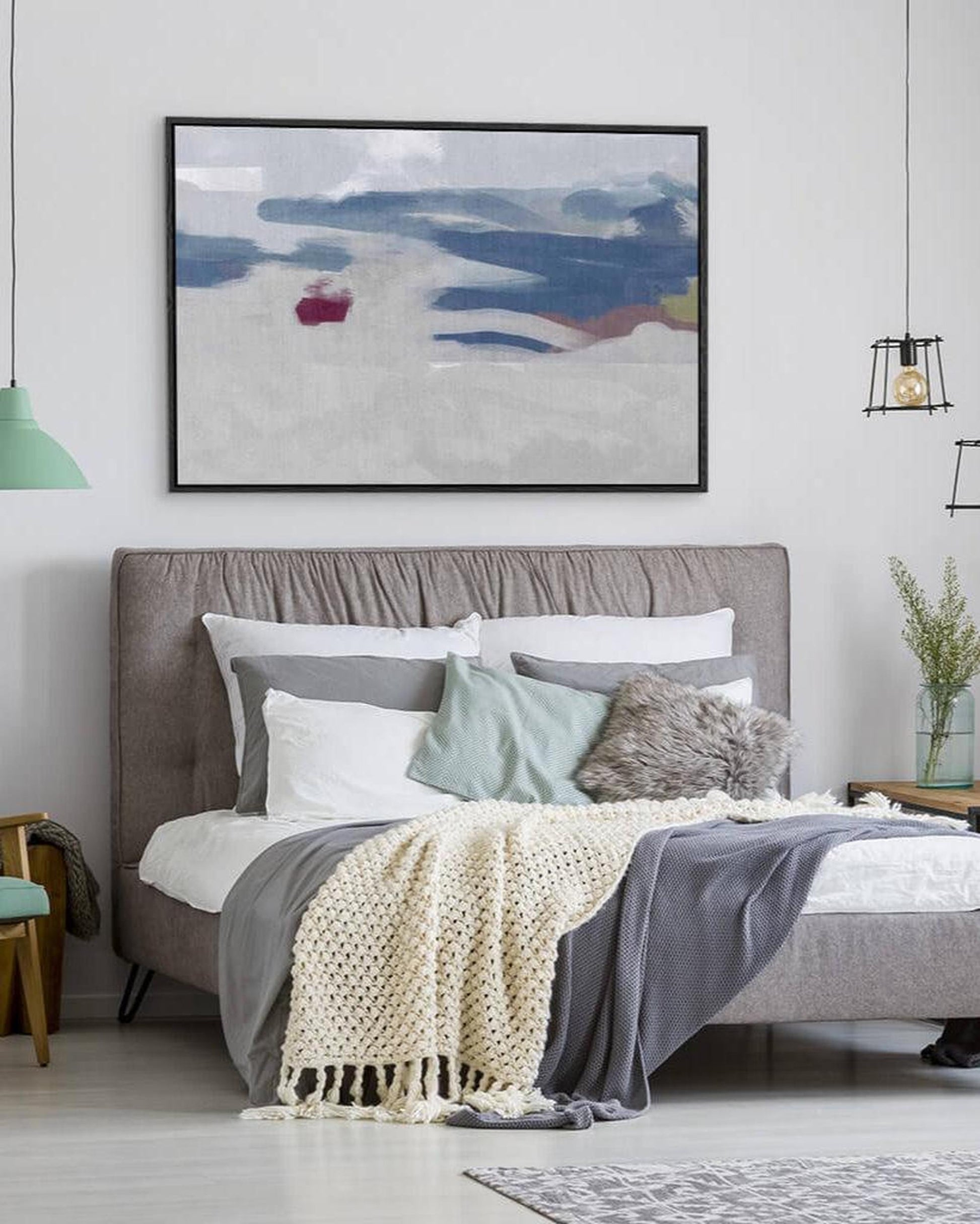 Modern bedroom with a bed, decorative pillows, and a framed abstract painting on the wall.