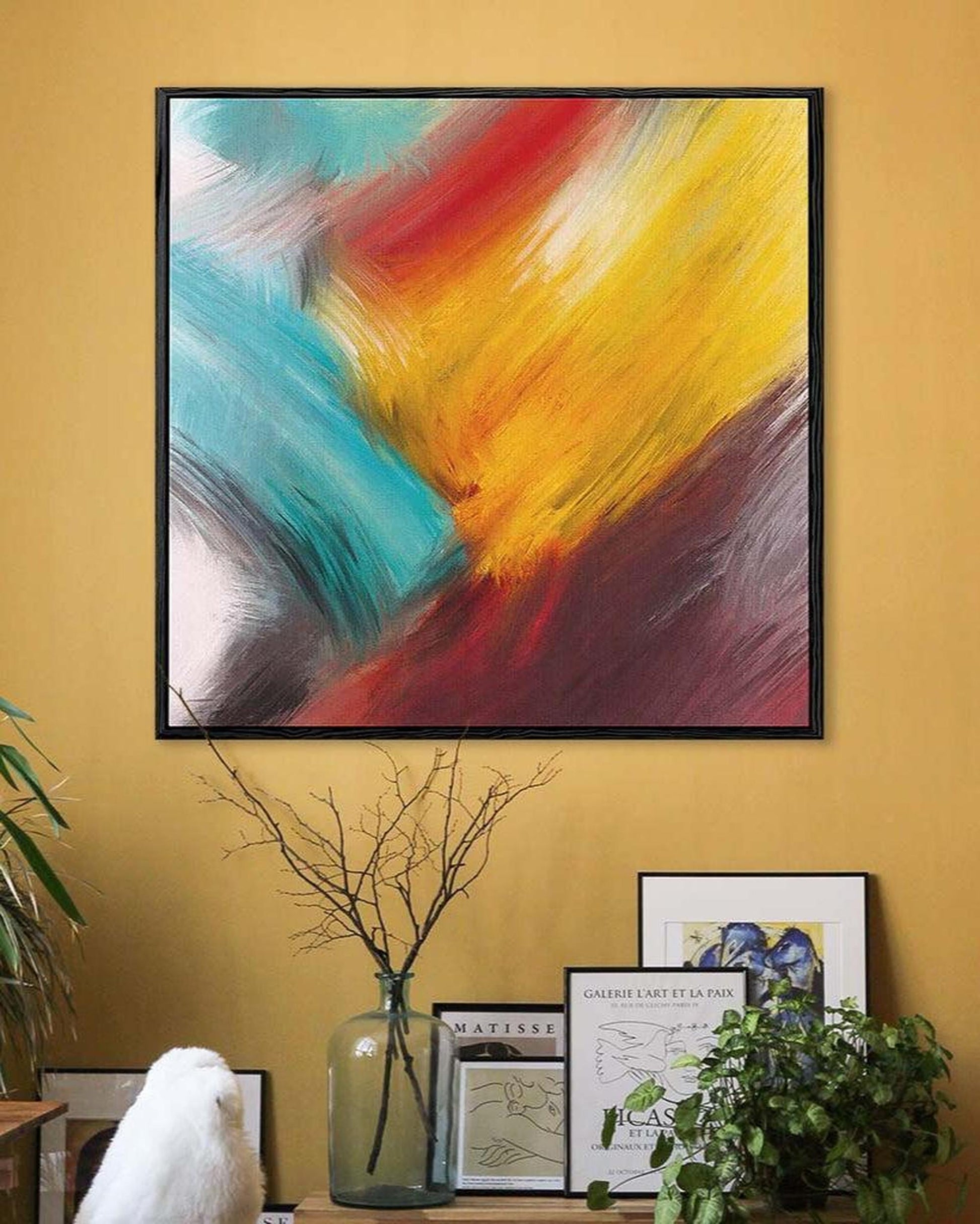 Abstract painting with vibrant colors on a yellow wall, surrounded by decor elements.
