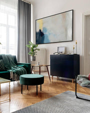 Modern living room with green sofa, round ottoman, and abstract painting on wall.