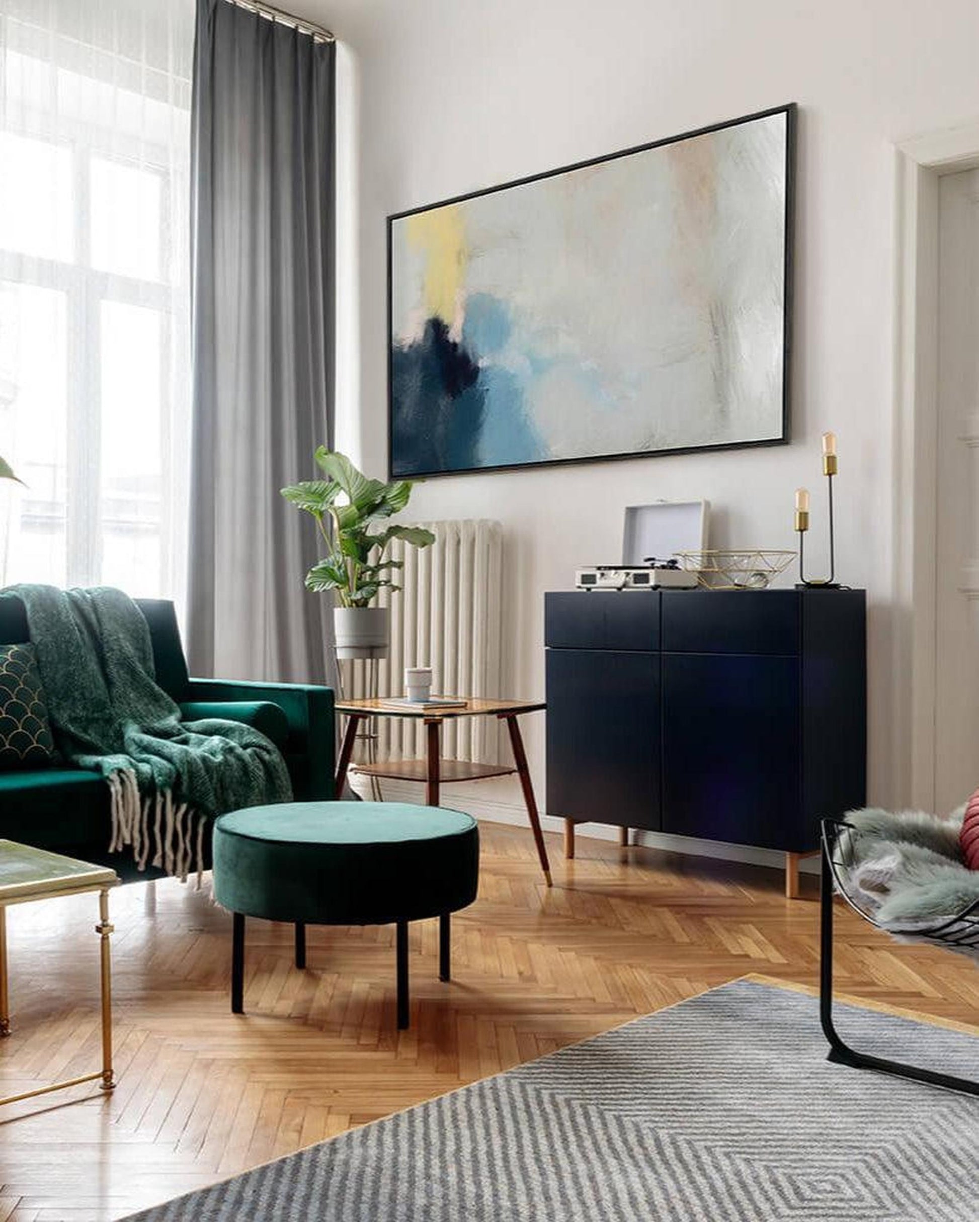 Modern living room with green sofa, round ottoman, and abstract painting on wall.