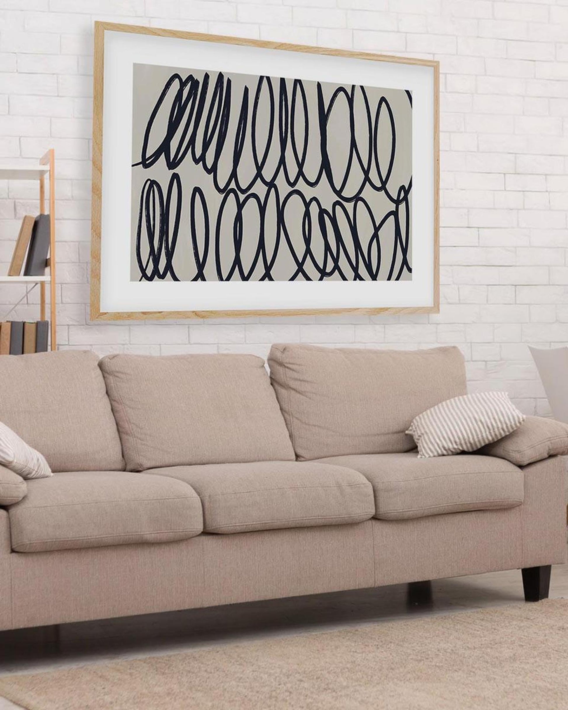 Beige sofa with a framed abstract art piece on a white brick wall.