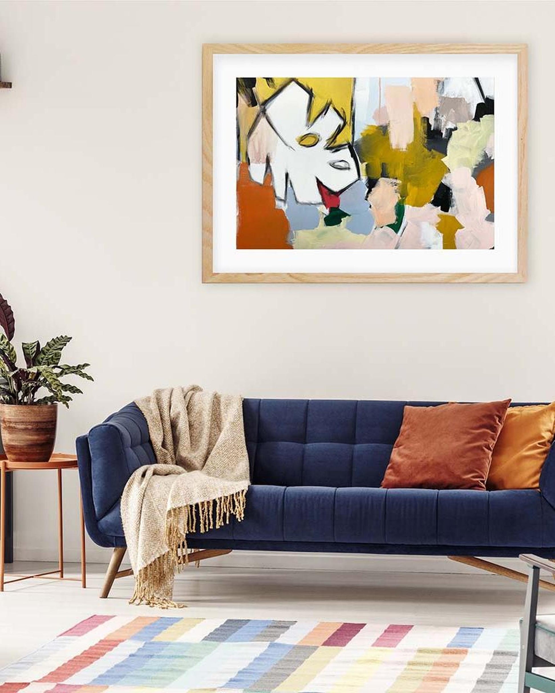 Framed abstract artwork above a blue sofa with colorful cushions in a living room.