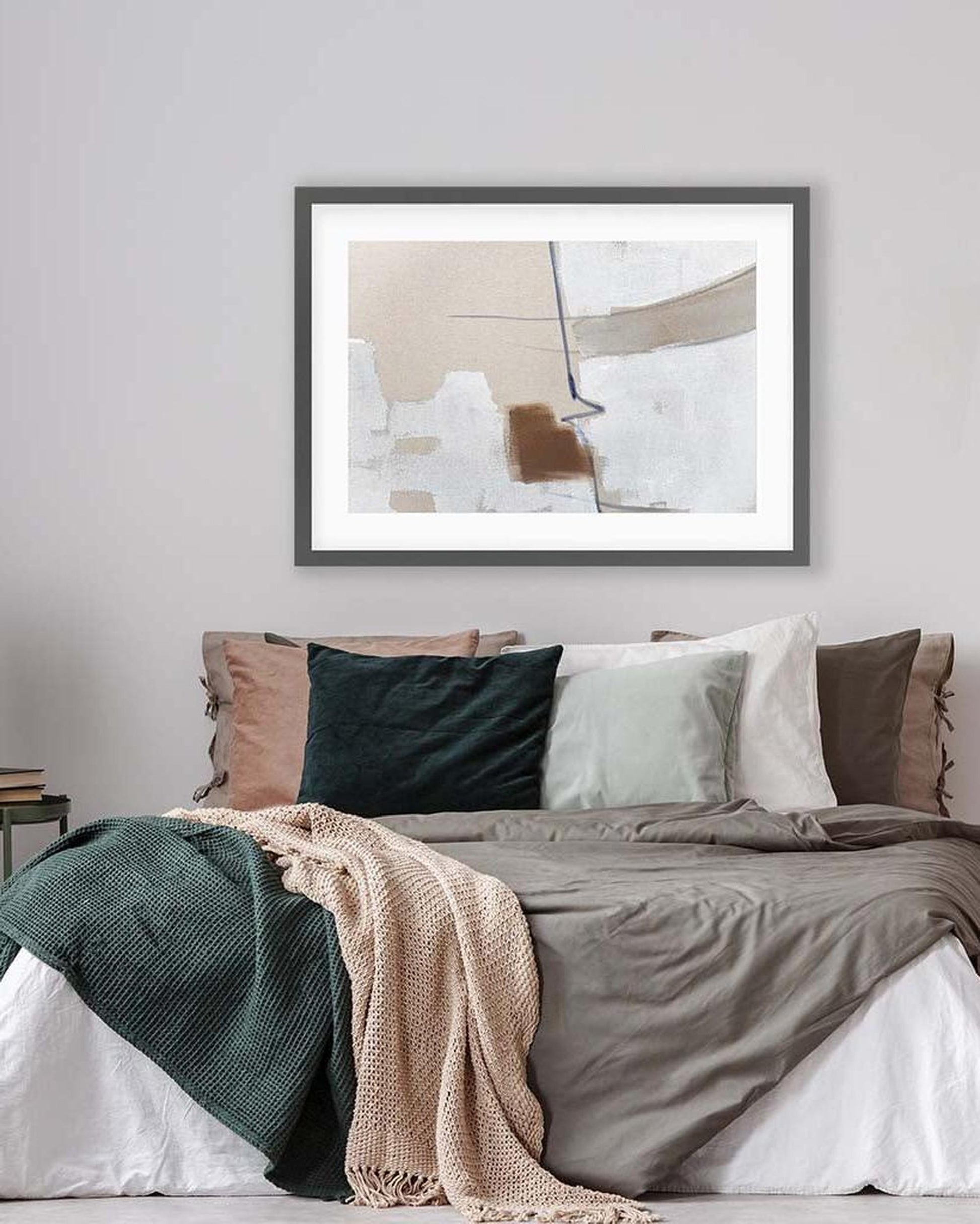 Framed abstract art above a bed with colorful bedding.
