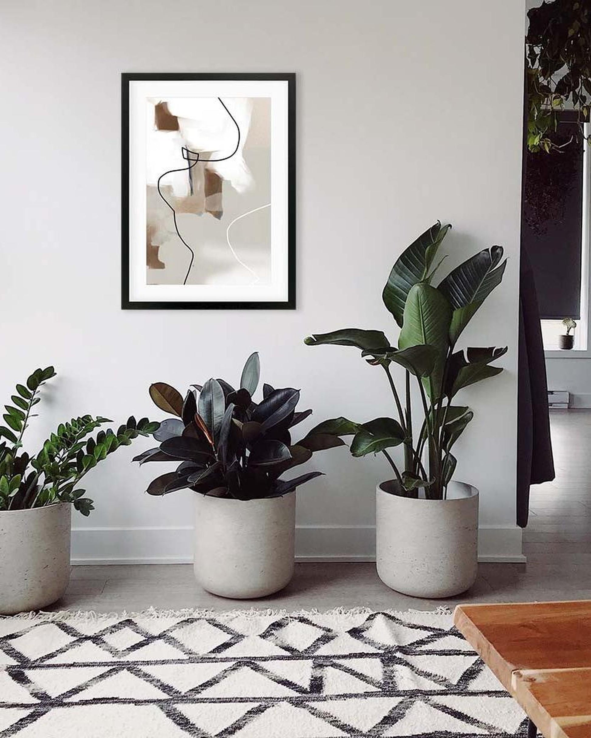 Living room with potted plants and a framed abstract art piece on the wall.