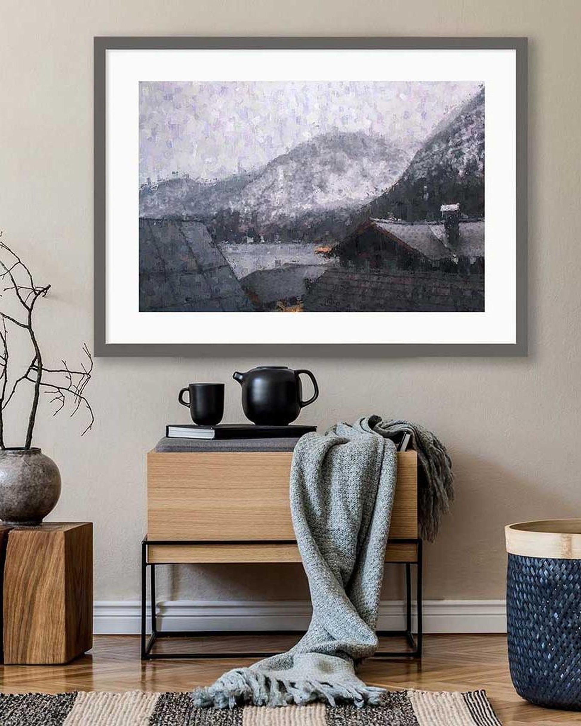 Framed mountain landscape print on a wall above a wooden side table with decorative items.