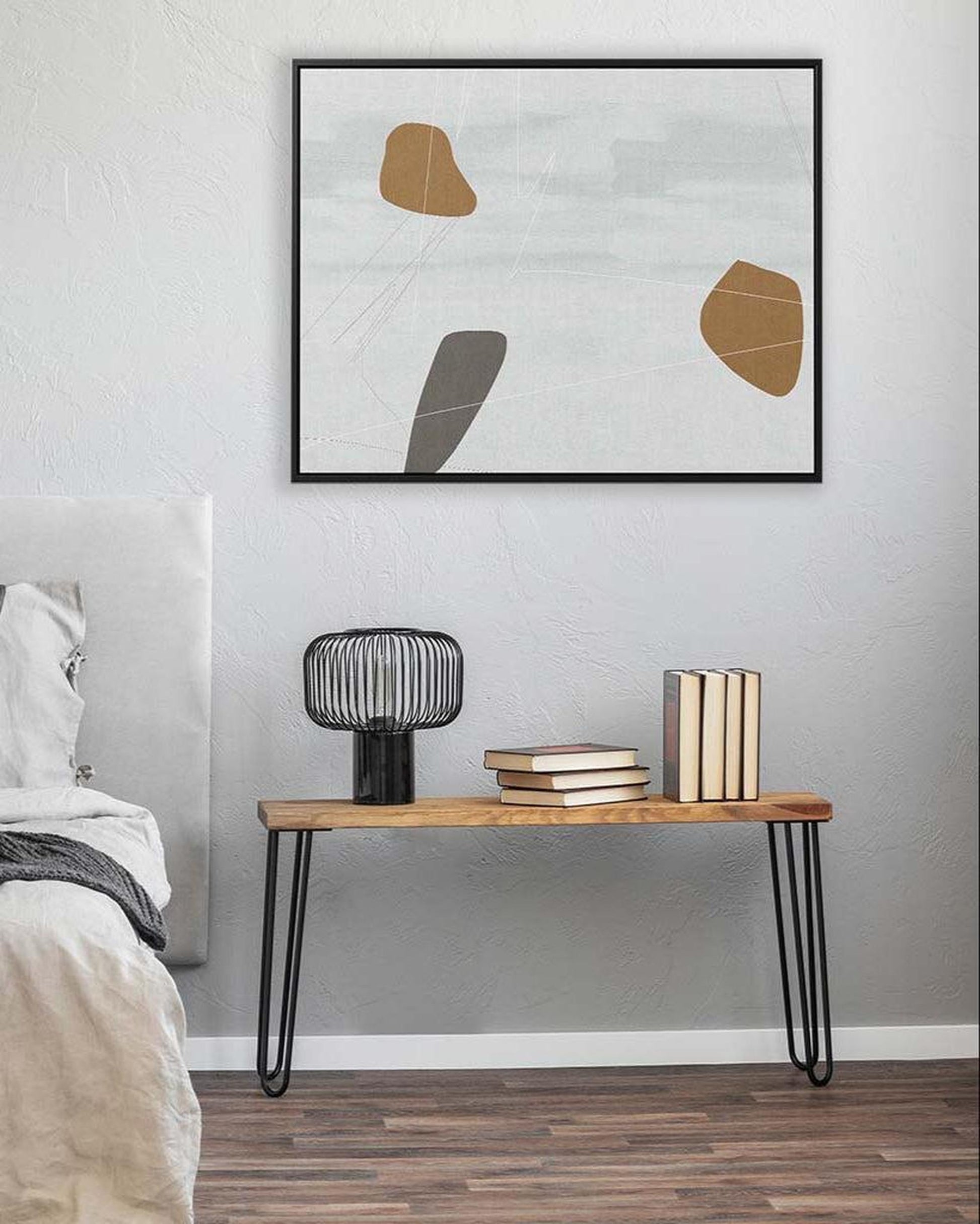 Modern bedroom with abstract art on the wall, wooden side table, and books.