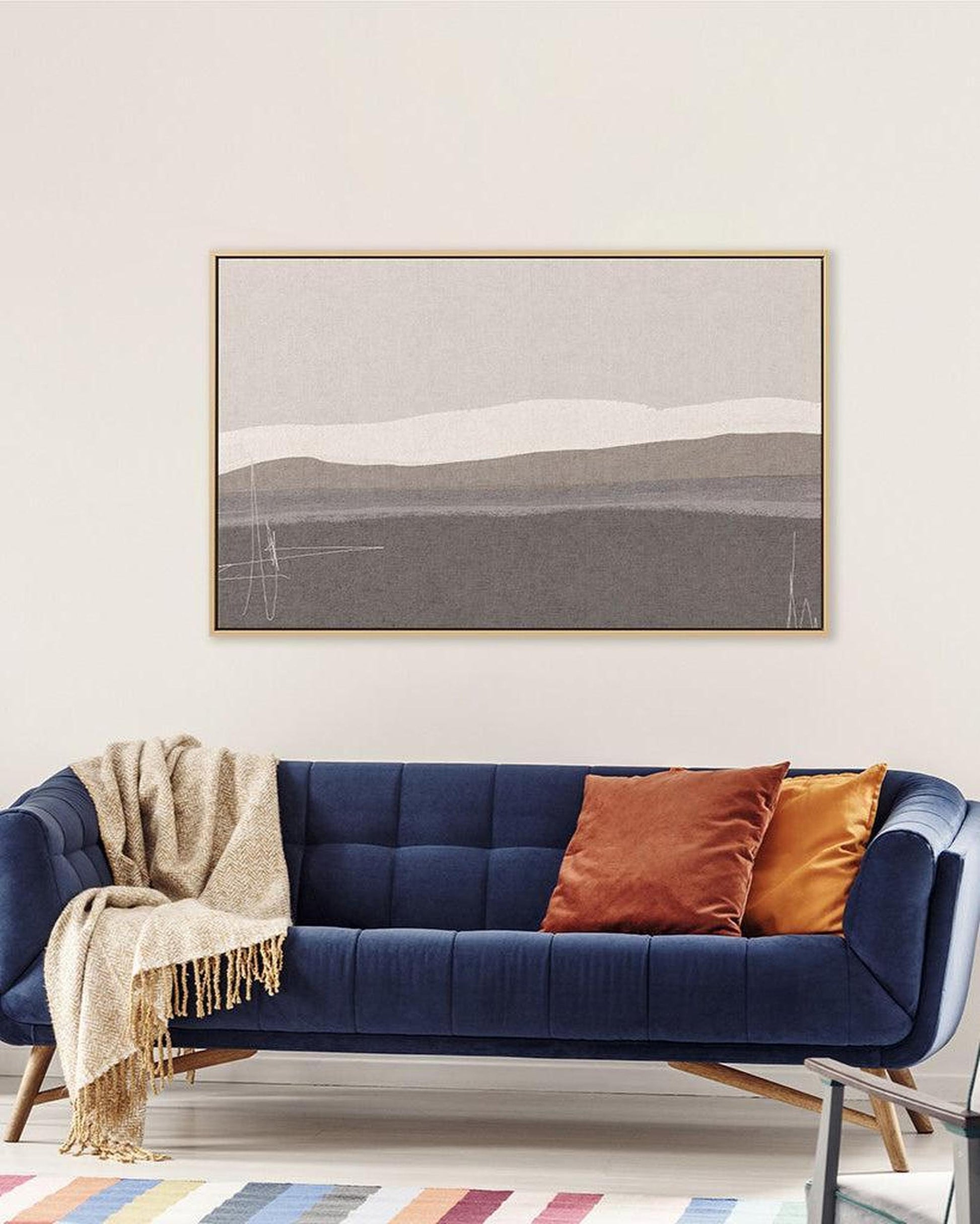 Navy blue sofa with colorful cushions and a framed landscape painting on the wall.