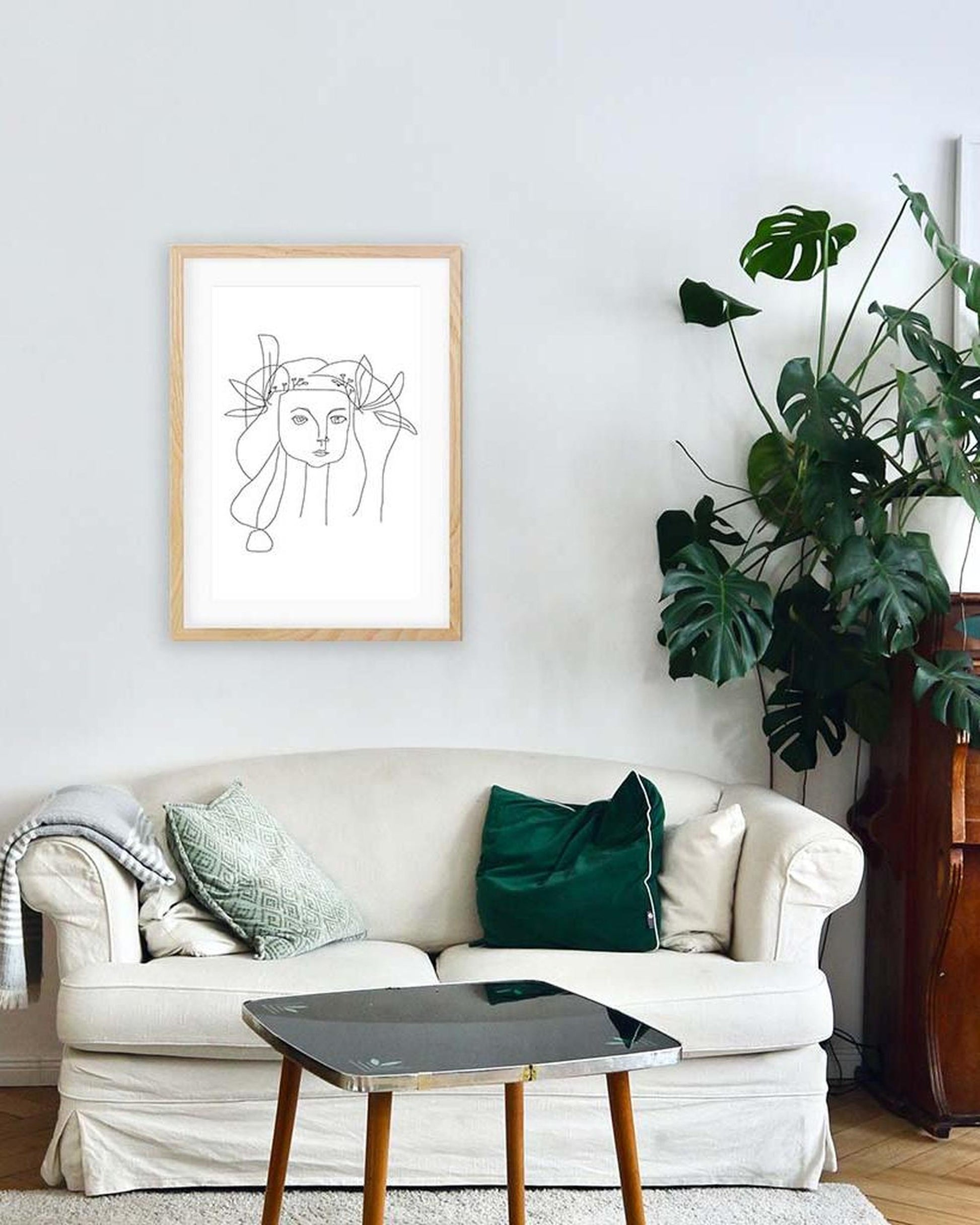 Living room with a white sofa, green cushions, a framed artwork, and a plant.