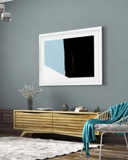 Framed abstract art on a gray wall above a wooden console table in a living room.
