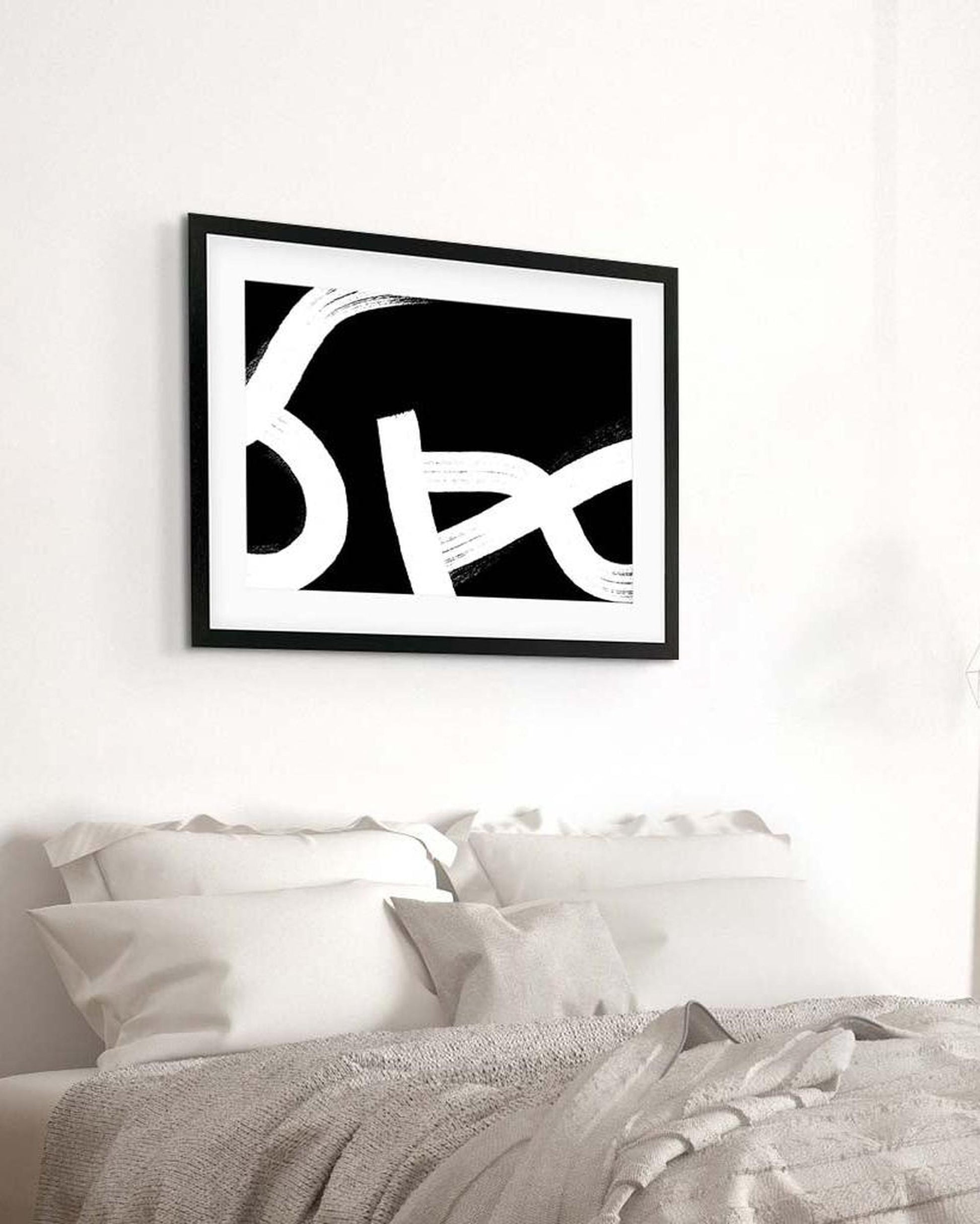 Framed black and white abstract art above a bed