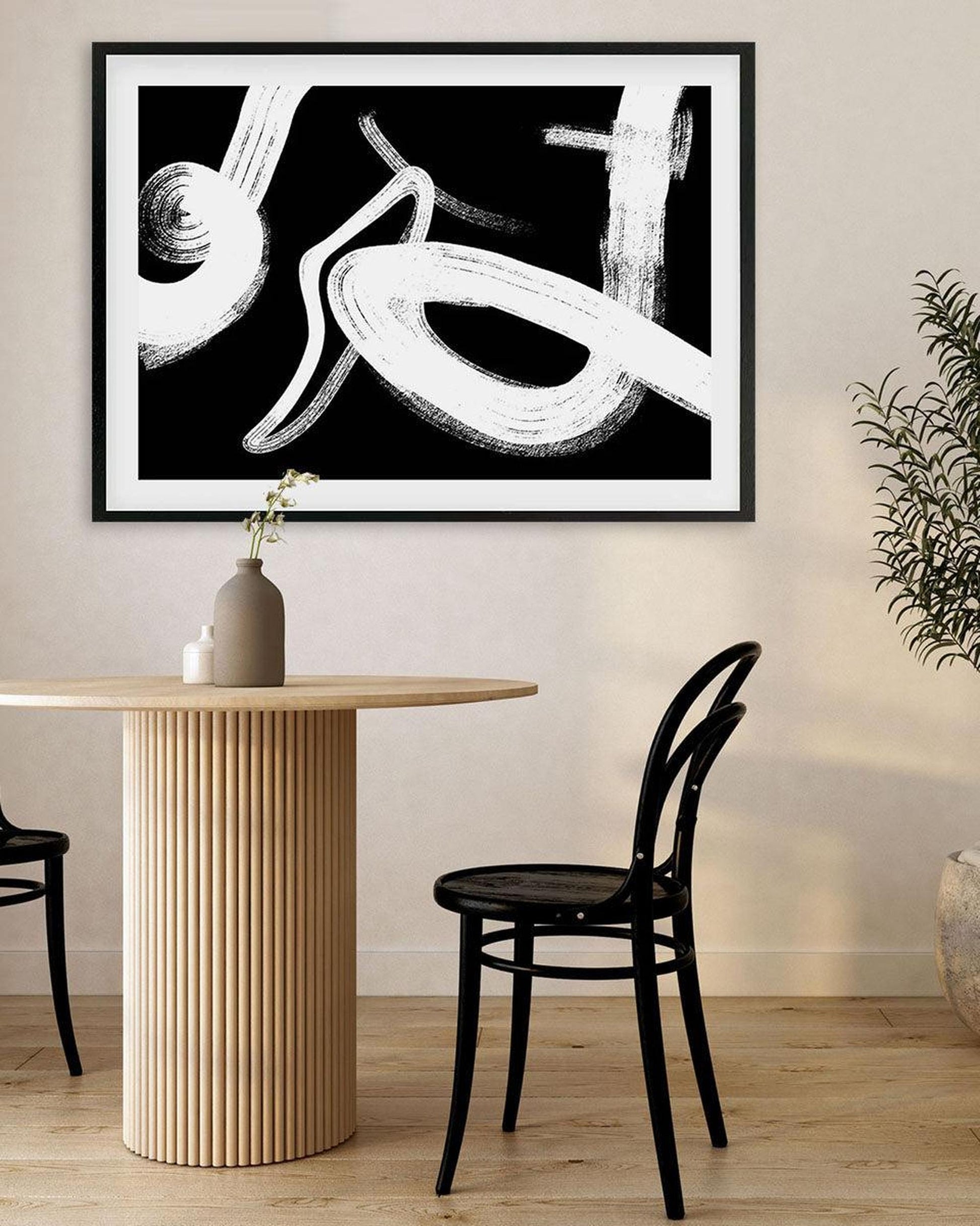 Abstract black and white painting on a wall above a dining table with a vase and chairs.