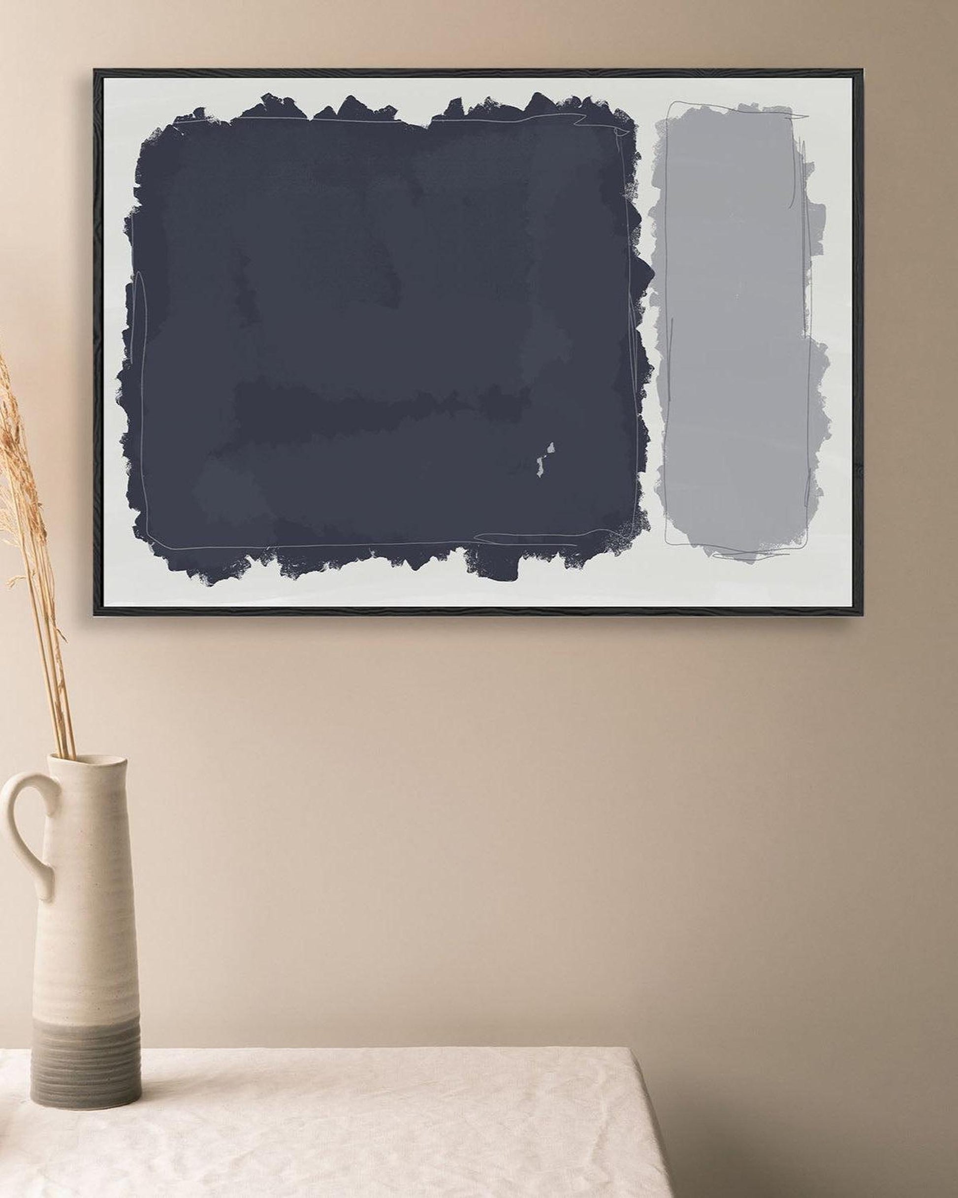 Abstract art print in a black frame on a beige wall with a vase below.