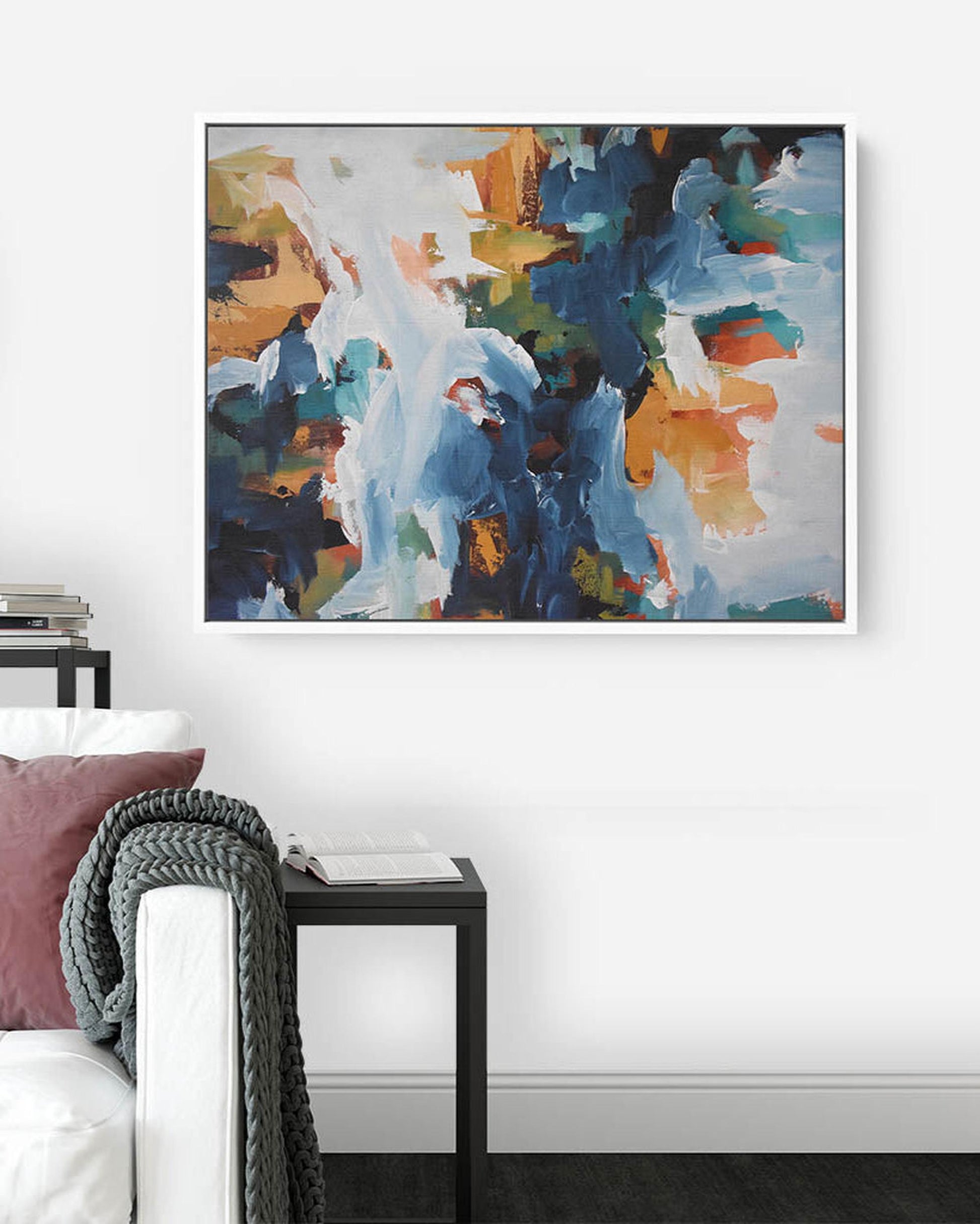 Abstract painting with blue, orange, and white colors on a white wall above a sofa.