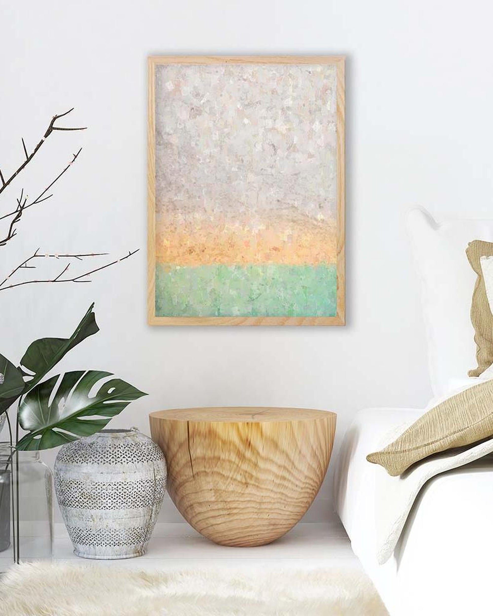 Abstract art piece on a wall with a wooden side table and plant in the foreground.