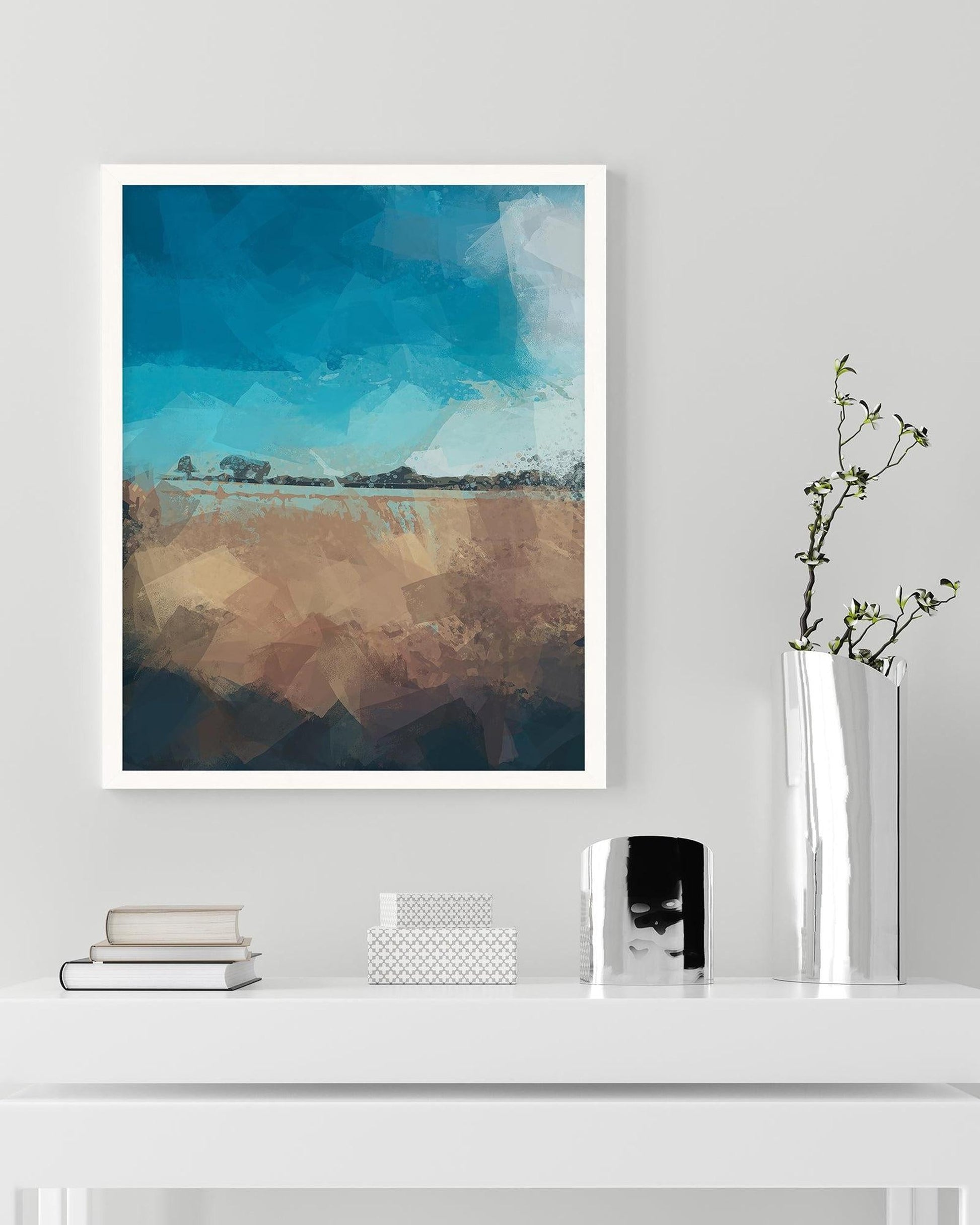 Framed abstract landscape art on a wall above a white shelf with decorative items.