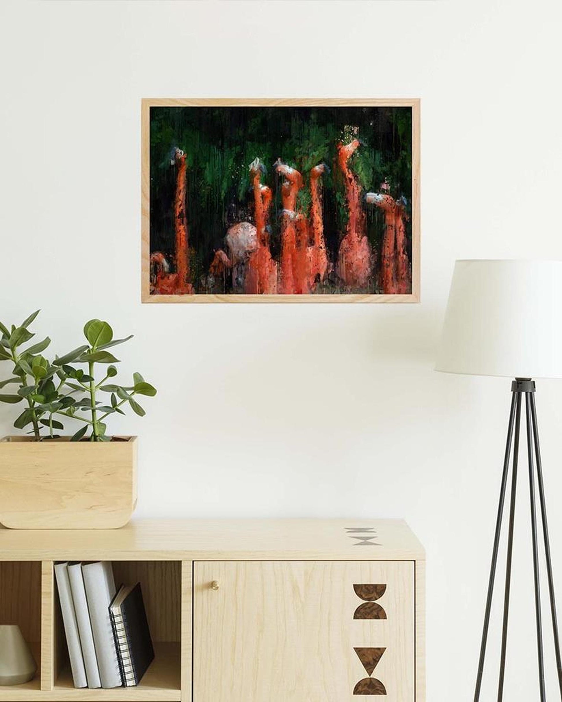 Framed artwork of flamingos on a wall above a wooden cabinet with decor items.