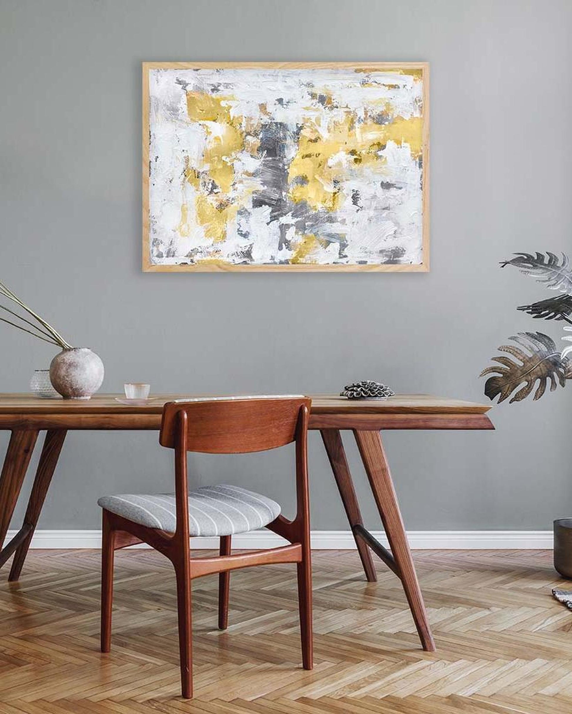 Wooden dining table with chair against a gray wall with abstract art