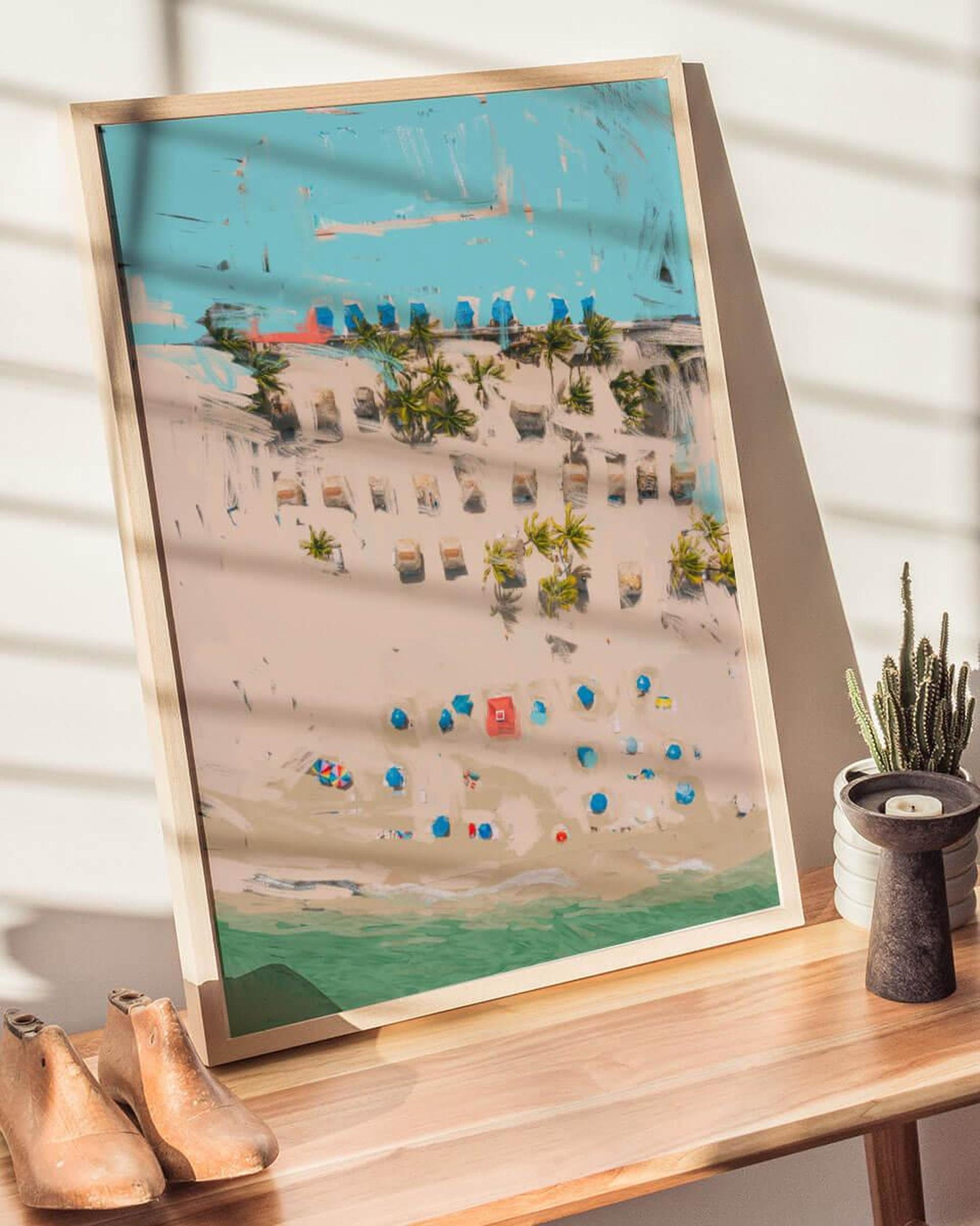 Framed artwork of a beach scene with buildings and palm trees on a wooden surface.