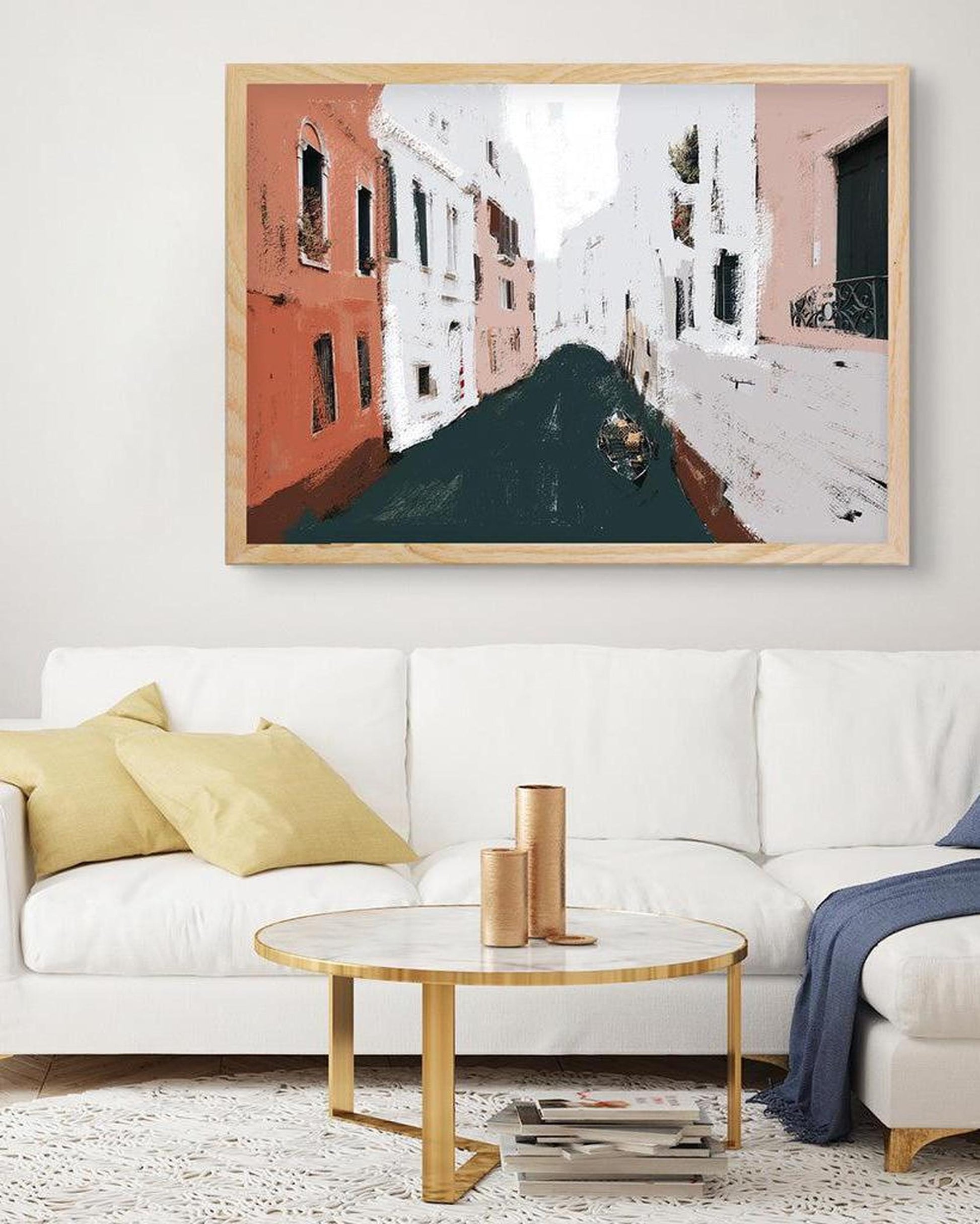 Framed artwork of a street scene above a white sofa with yellow pillows in a living room.