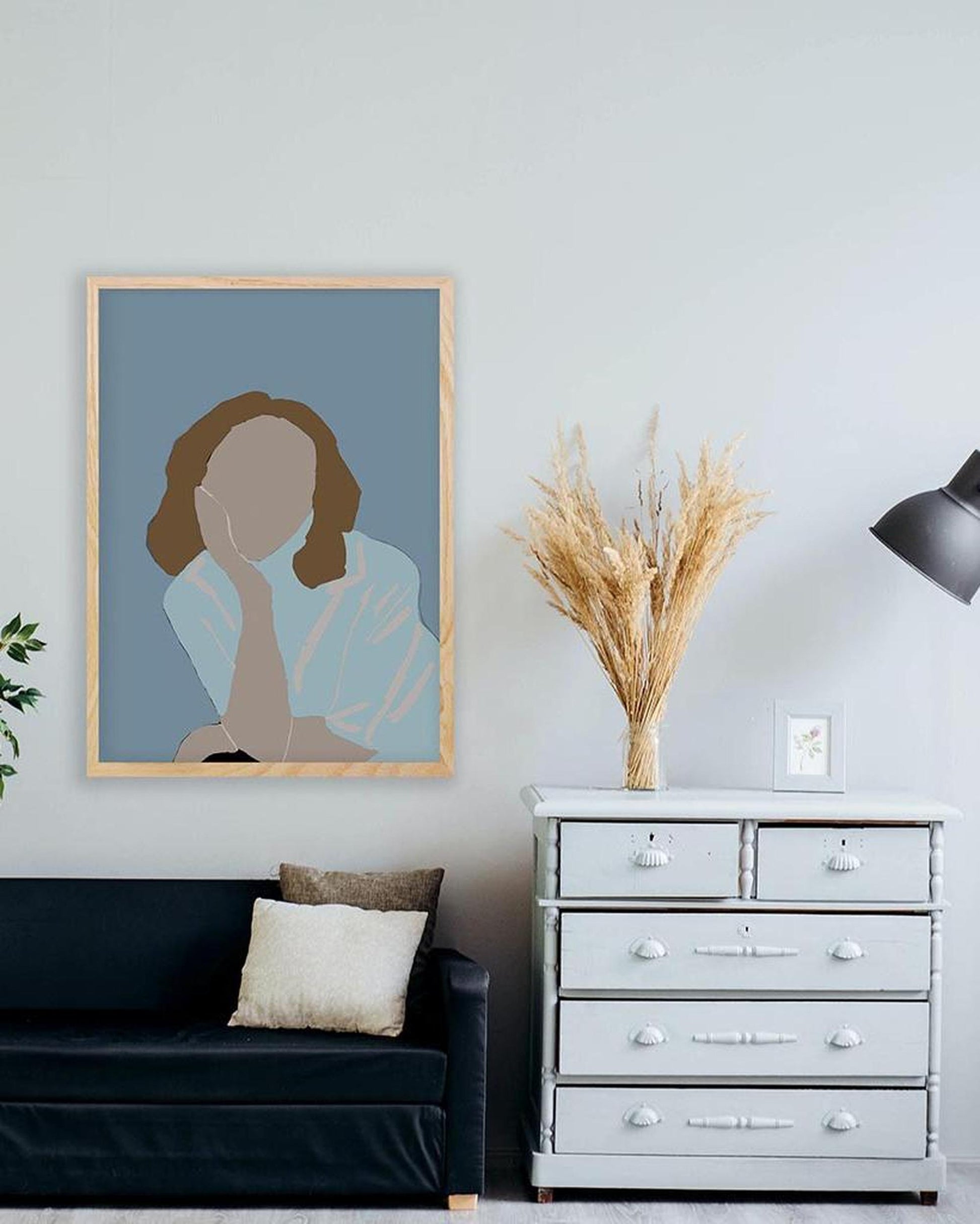 Living room with a framed portrait on the wall, a black sofa, and a white dresser.