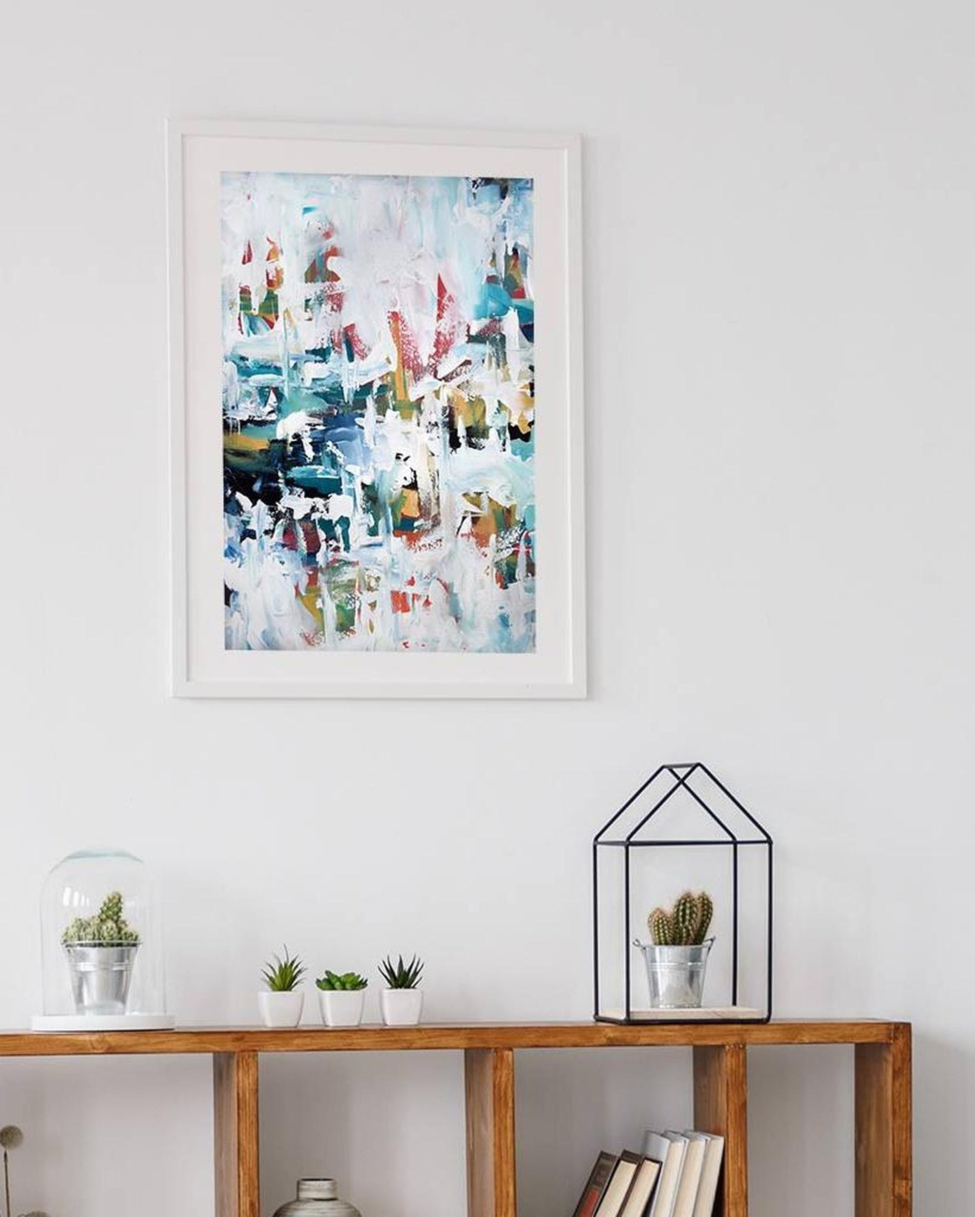 Framed abstract art piece on a wall above a wooden console table with decorative items.