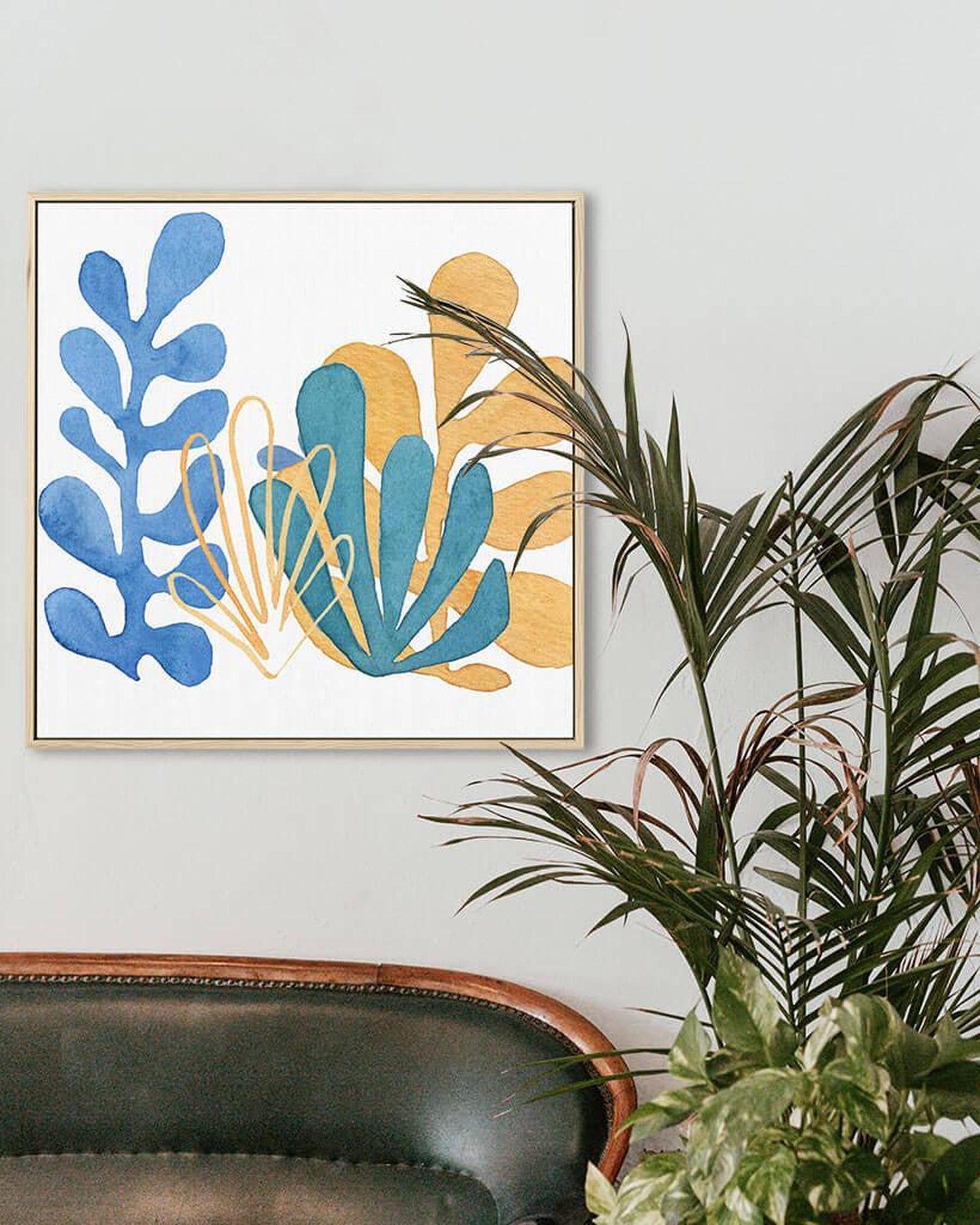 A canvas print featuring an abstract design with blue, yellow, and brown colors, framed and hanging on a wall above a plant.