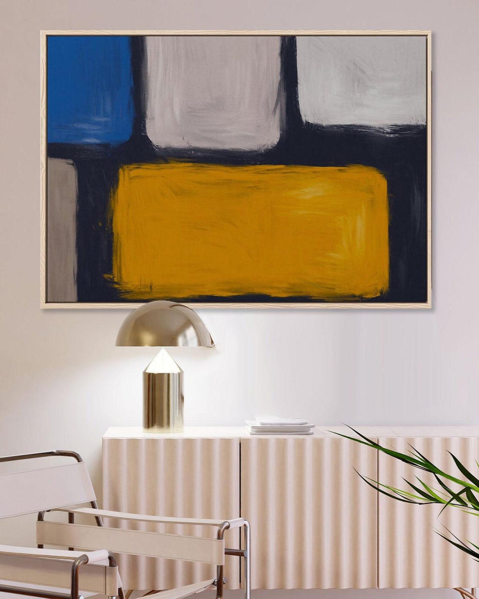 Abstract art piece with blue, white, and yellow colors on a wall above a table and chair.
