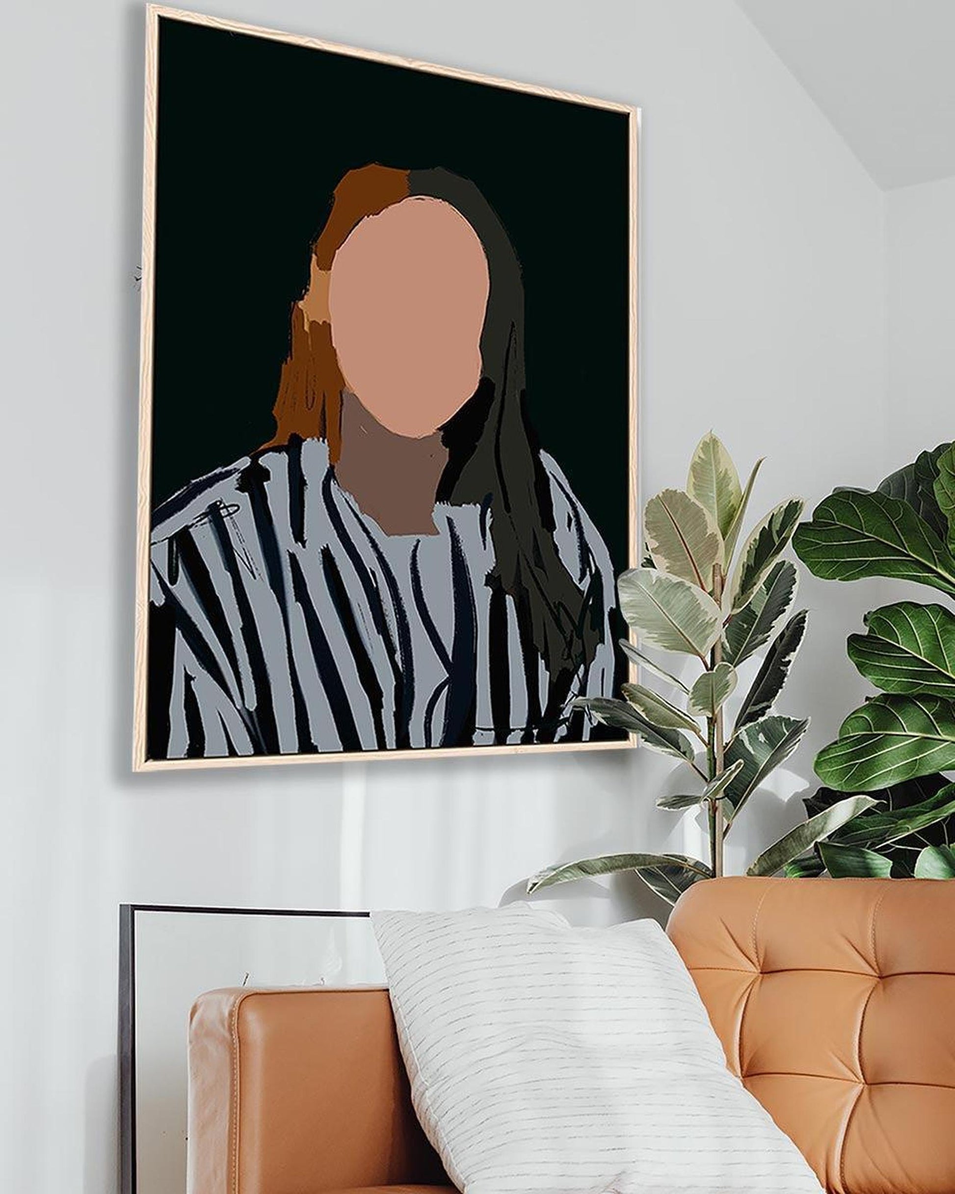 Framed abstract art piece on a wall with a plant and brown sofa in the foreground.