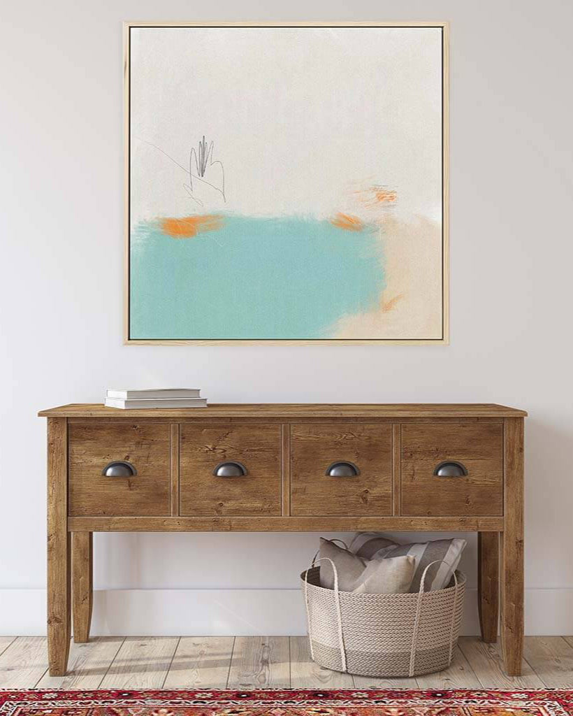 Wooden console table with a basket and books underneath, framed abstract art above on a white wall.