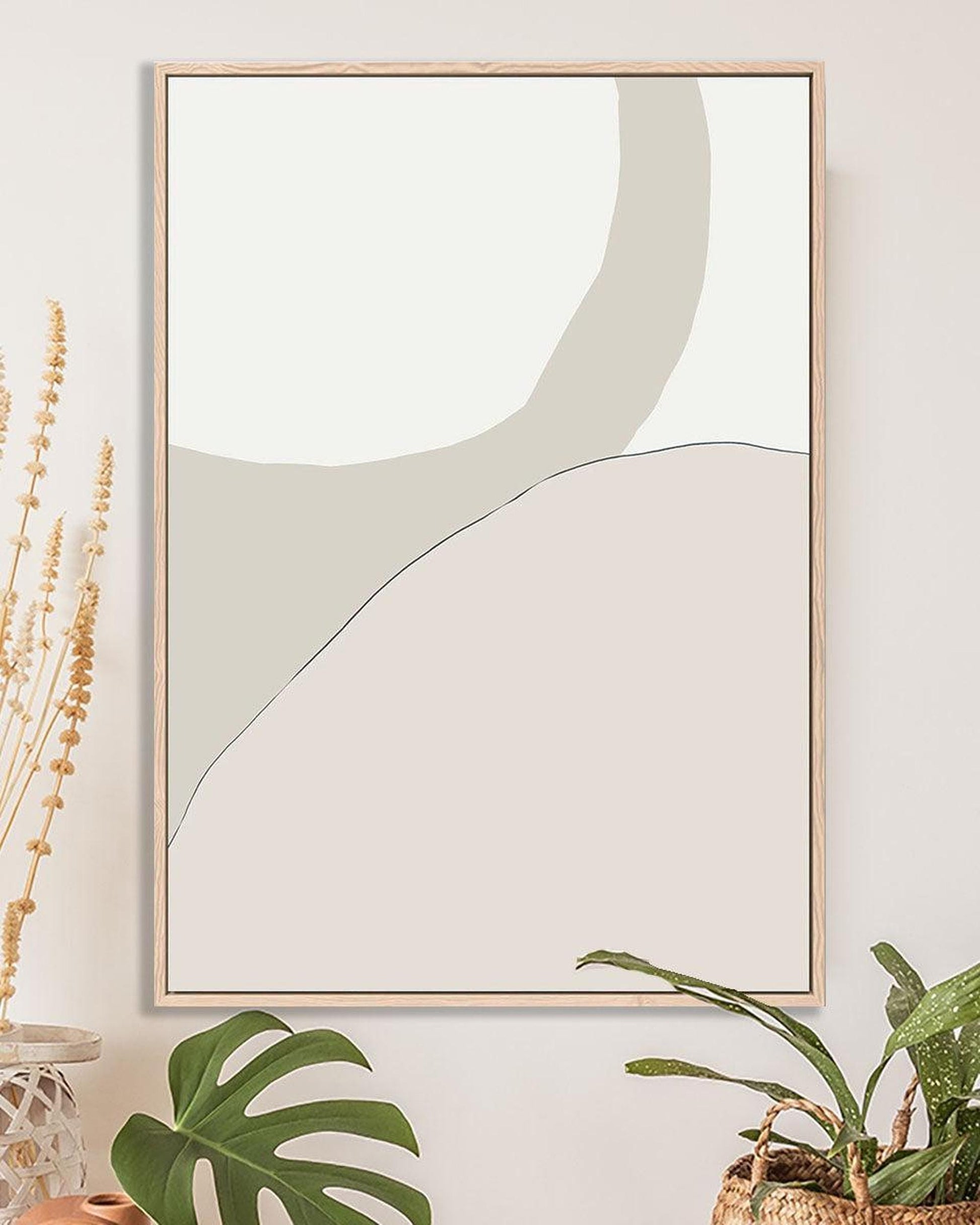 Framed abstract art piece on a wall with plants and decor items below.