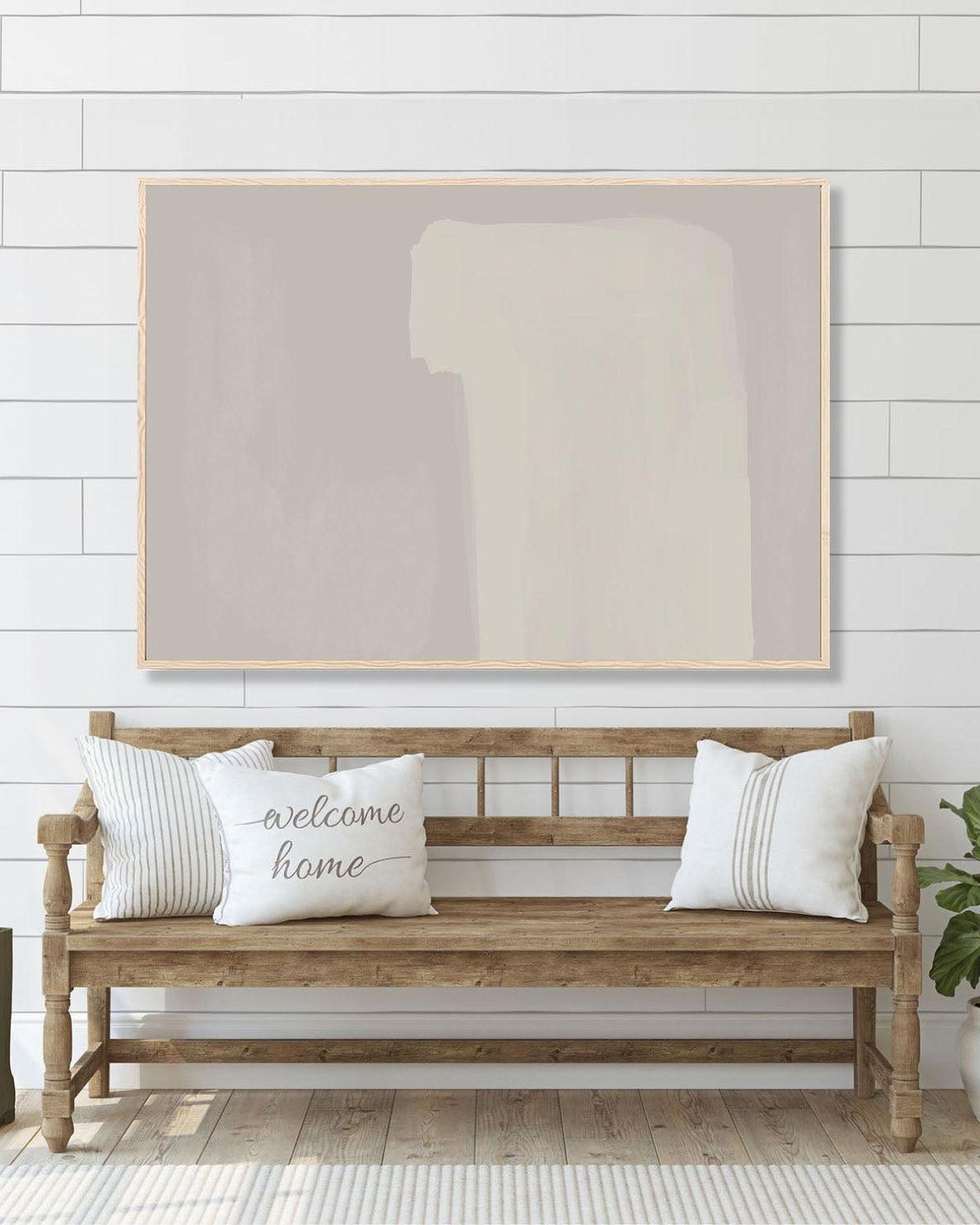 Wooden bench with 'welcome home' pillows under a large abstract painting on a white wall.