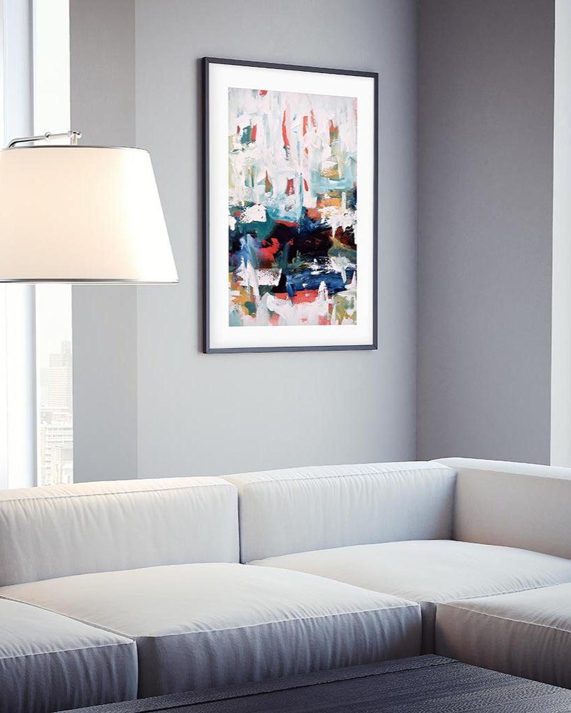 Framed abstract art piece on a gray wall above a white sofa.