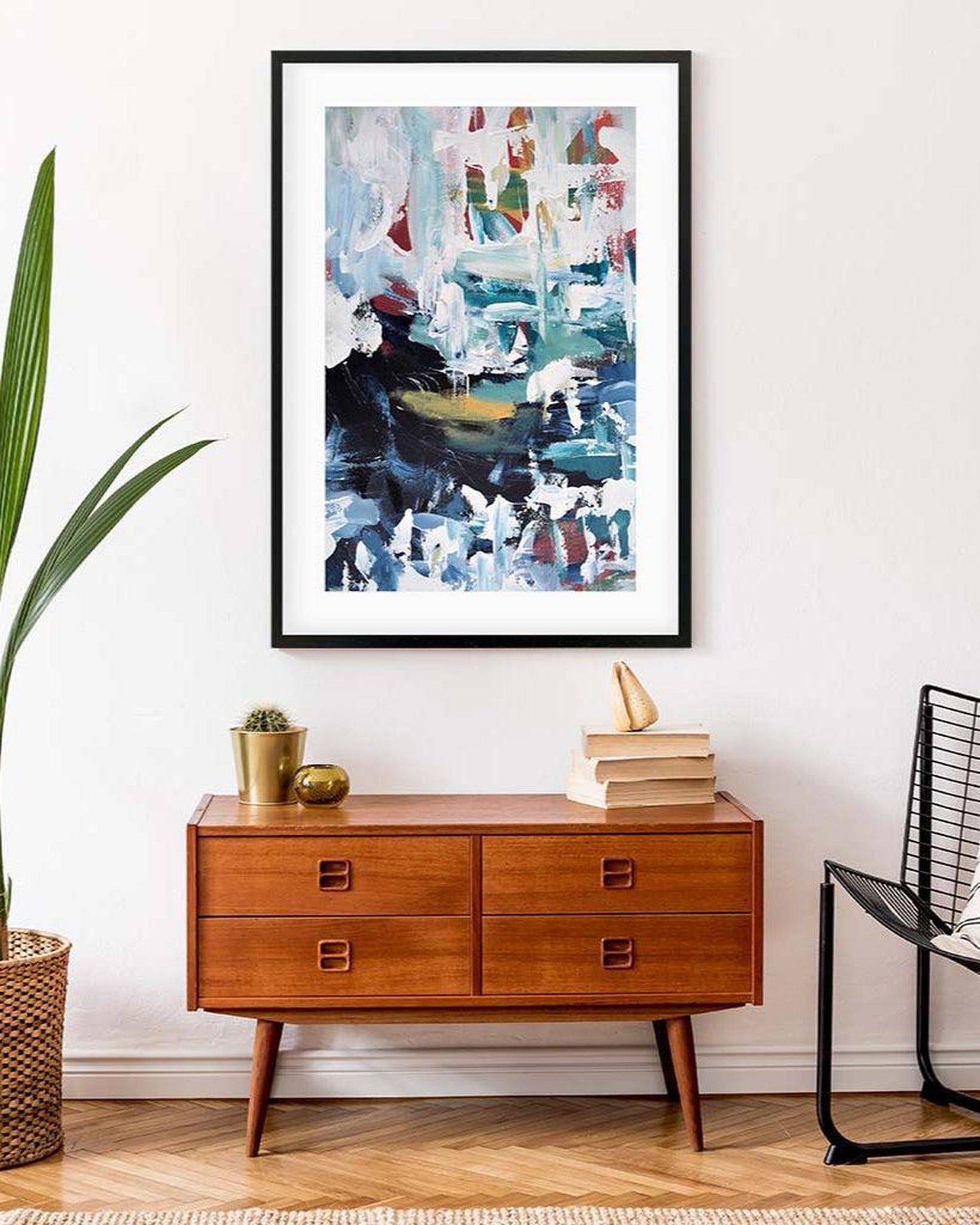 Abstract art print on a wall above a wooden dresser with decorative items.