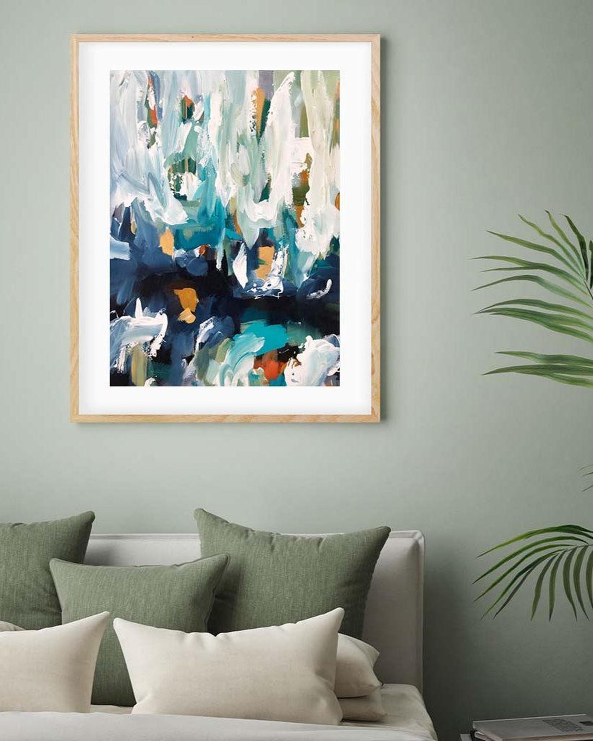 Framed abstract art on a wall above a bed with green and beige pillows.