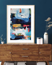 Framed abstract art on a blue wall above a wooden cabinet.