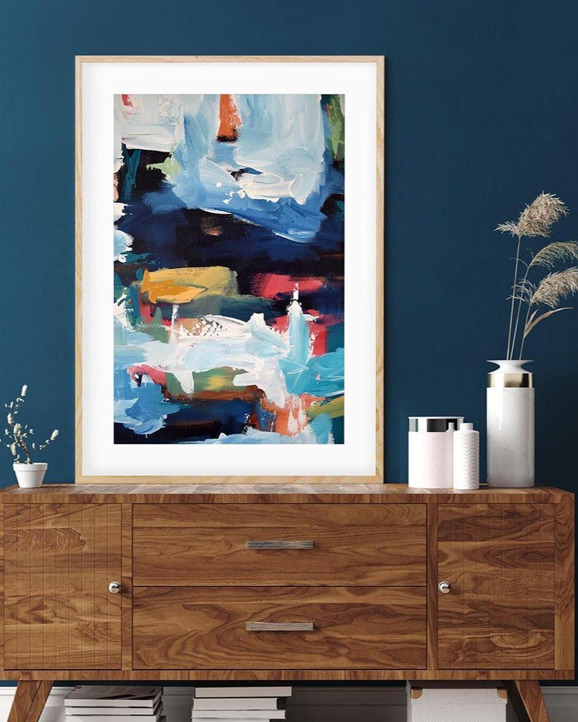 Framed abstract art on a blue wall above a wooden cabinet.