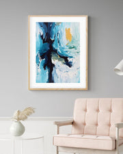 Abstract art print in a wooden frame on a gray wall above a beige sofa.