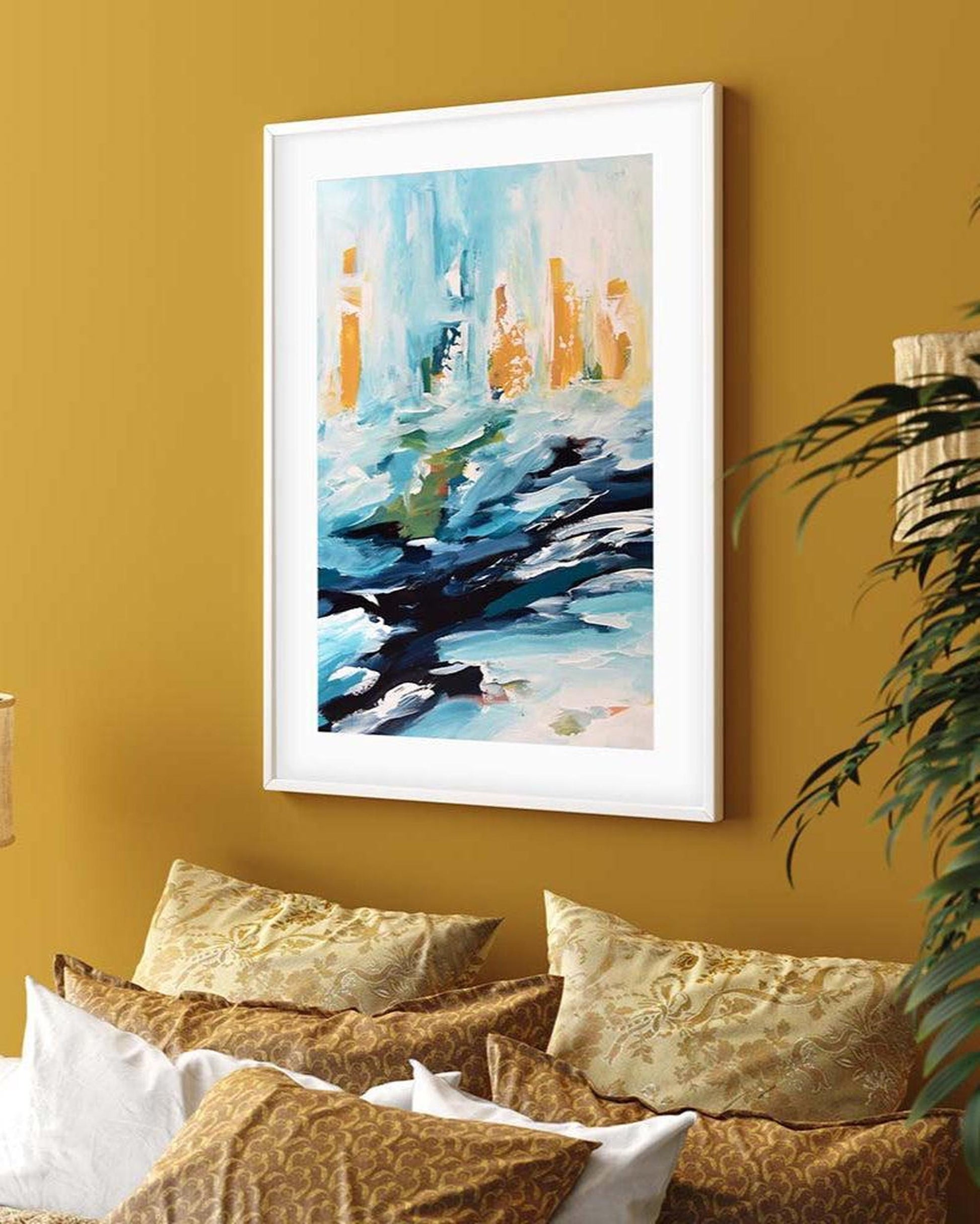 Framed abstract painting on a mustard yellow wall above a sofa with patterned cushions.