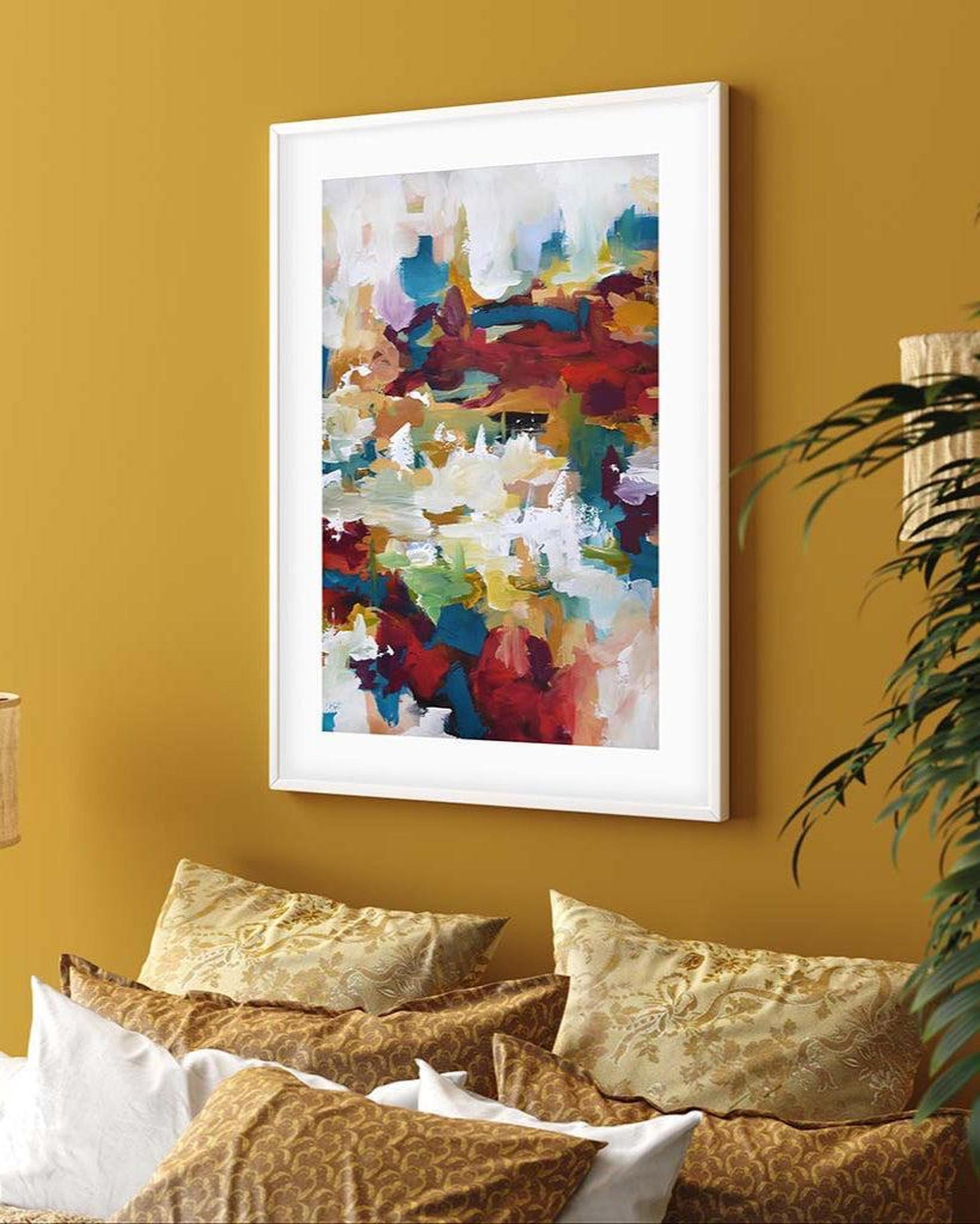 Framed abstract art on a yellow wall above a bed with gold bedding.