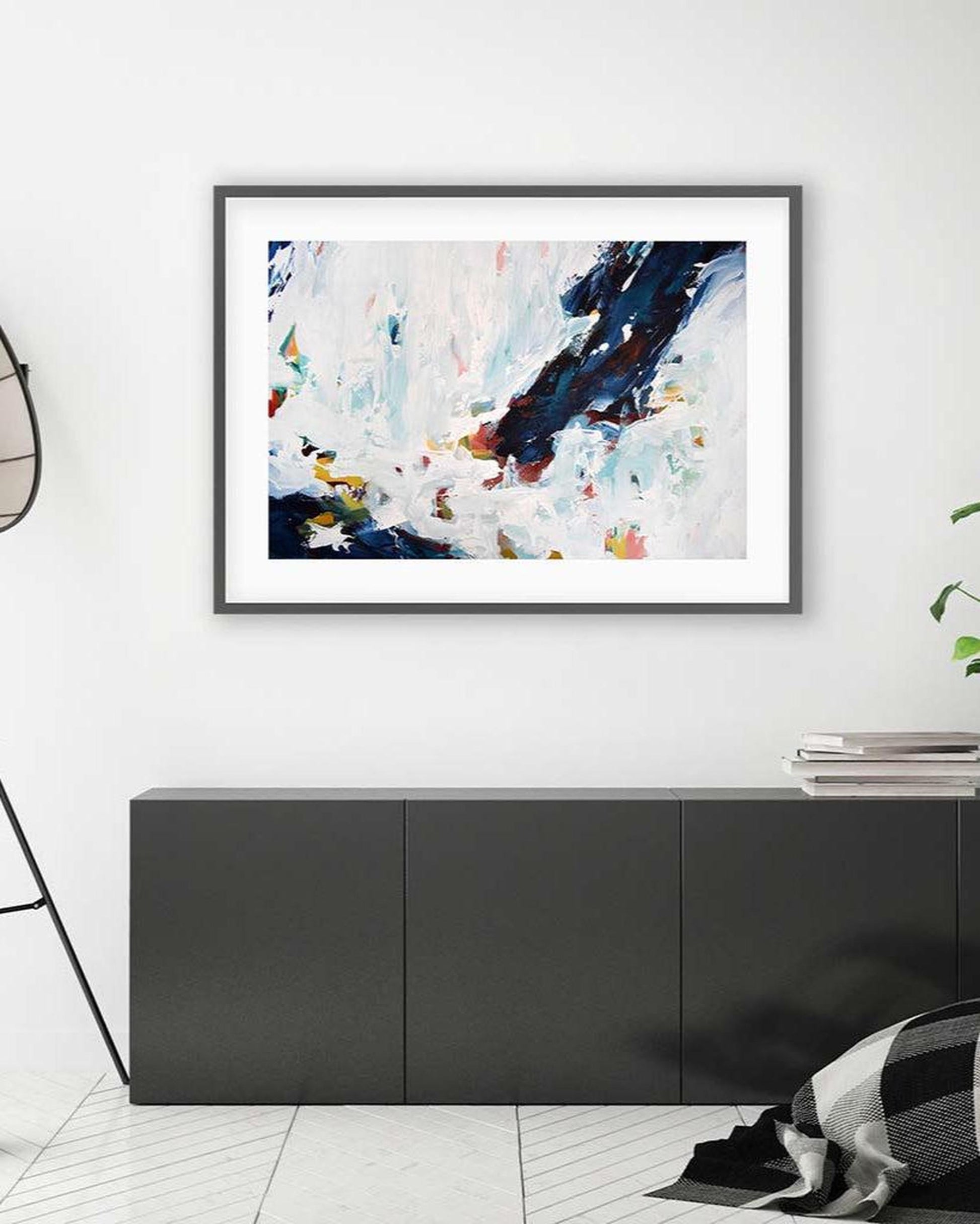 Framed abstract art piece on a white wall above a black cabinet.