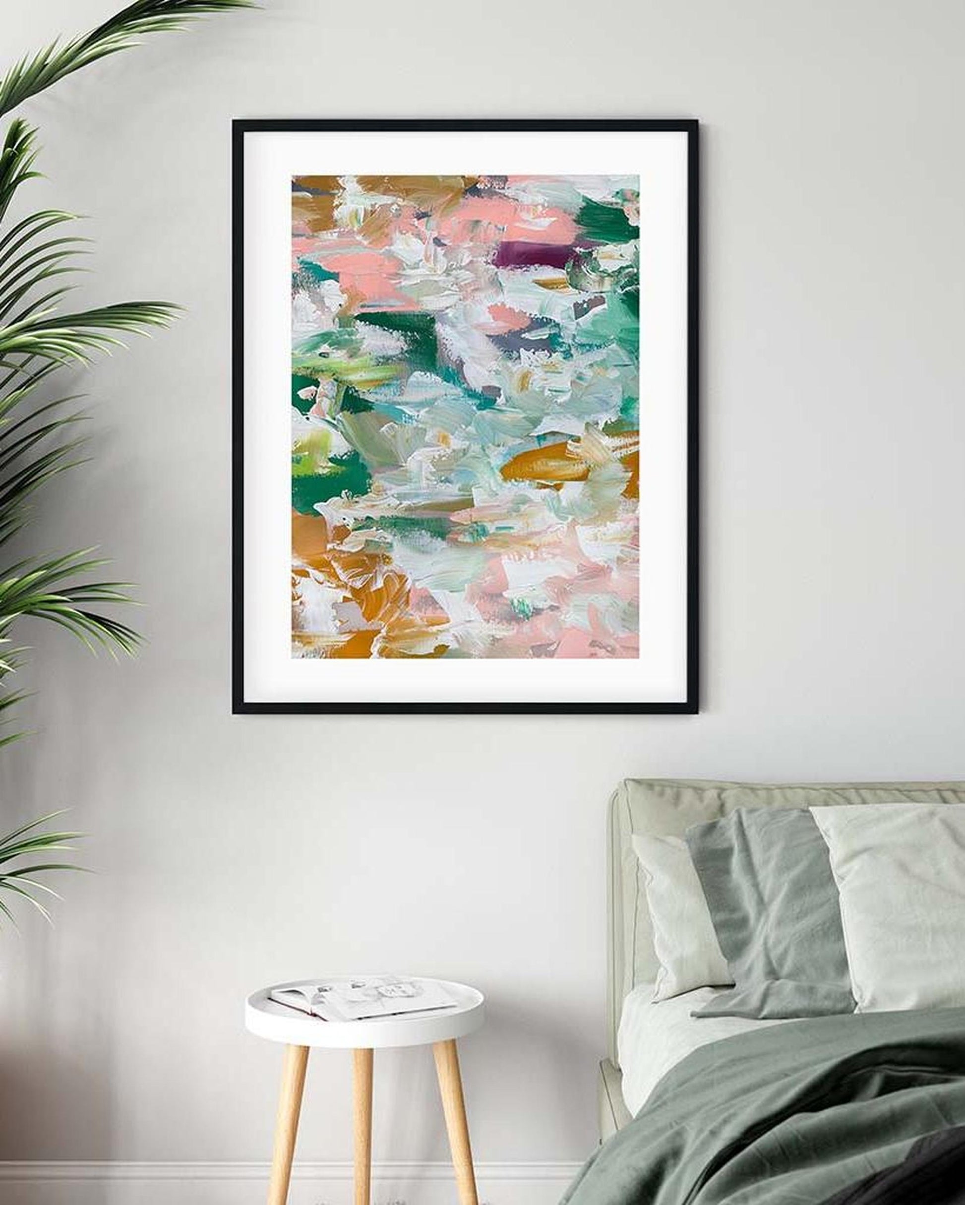 Abstract art print in a black frame on a wall above a bed.
