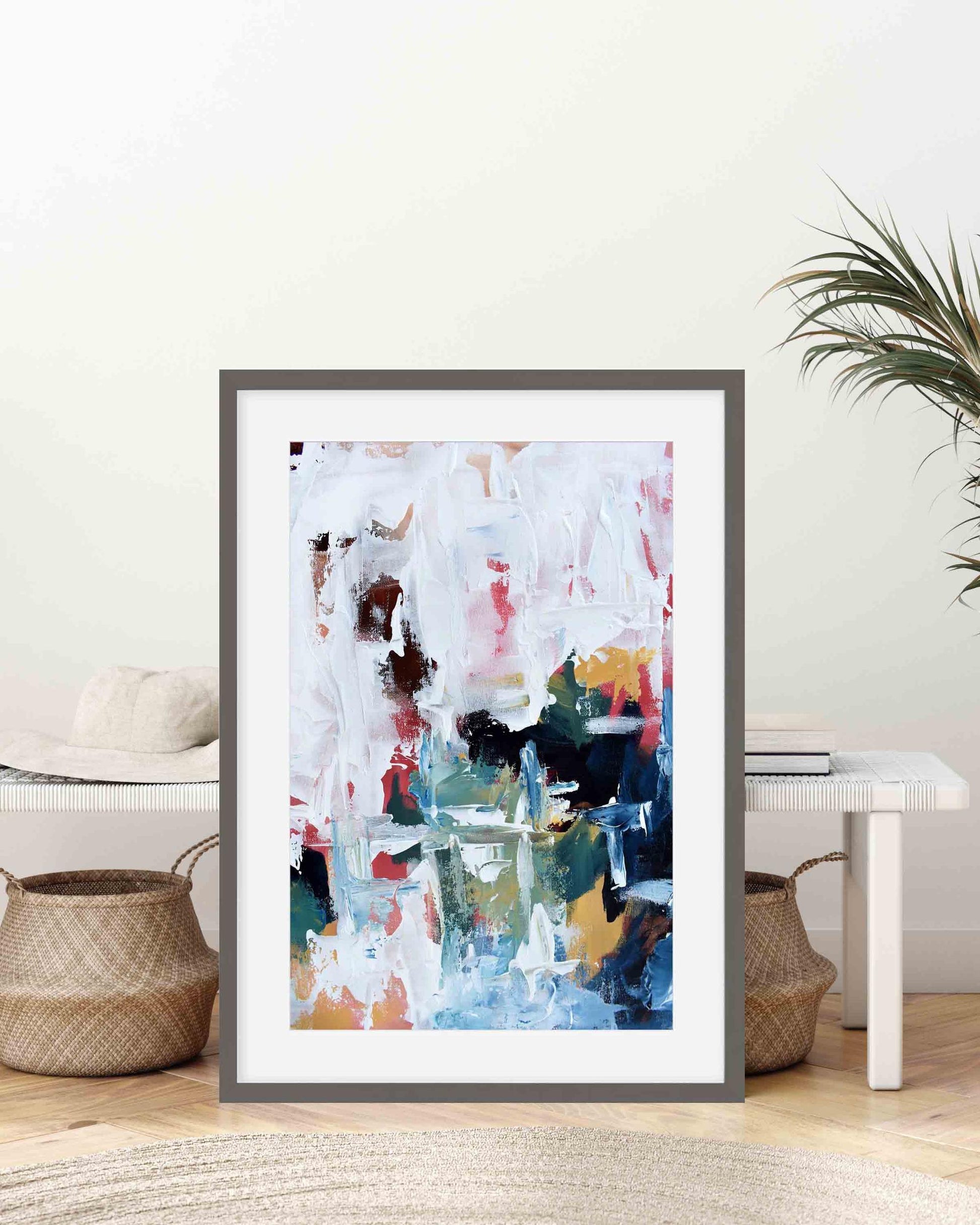 Framed abstract art print on a wall with a plant and decor items below.
