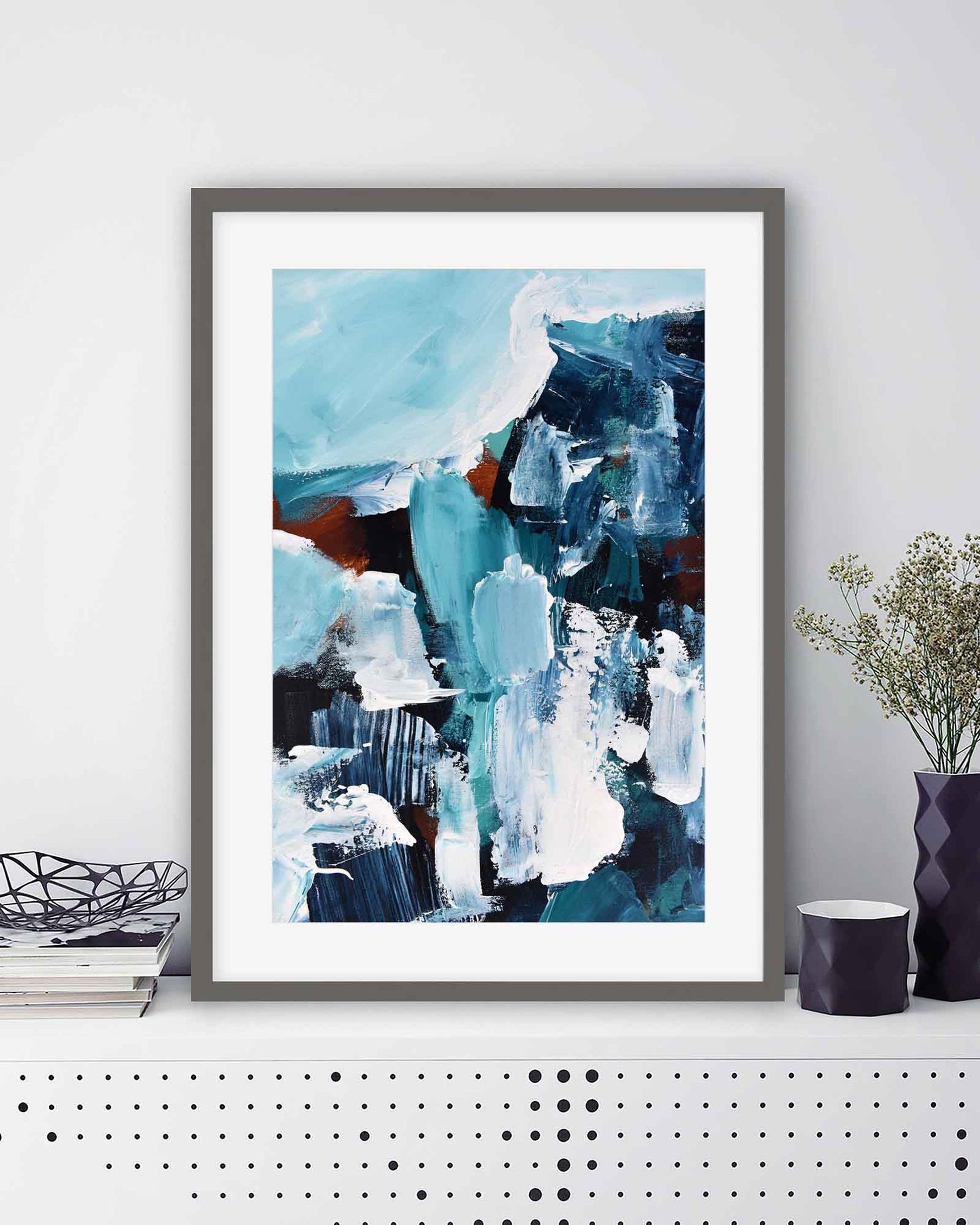 Framed abstract art print with blue and white colors on a white wall.