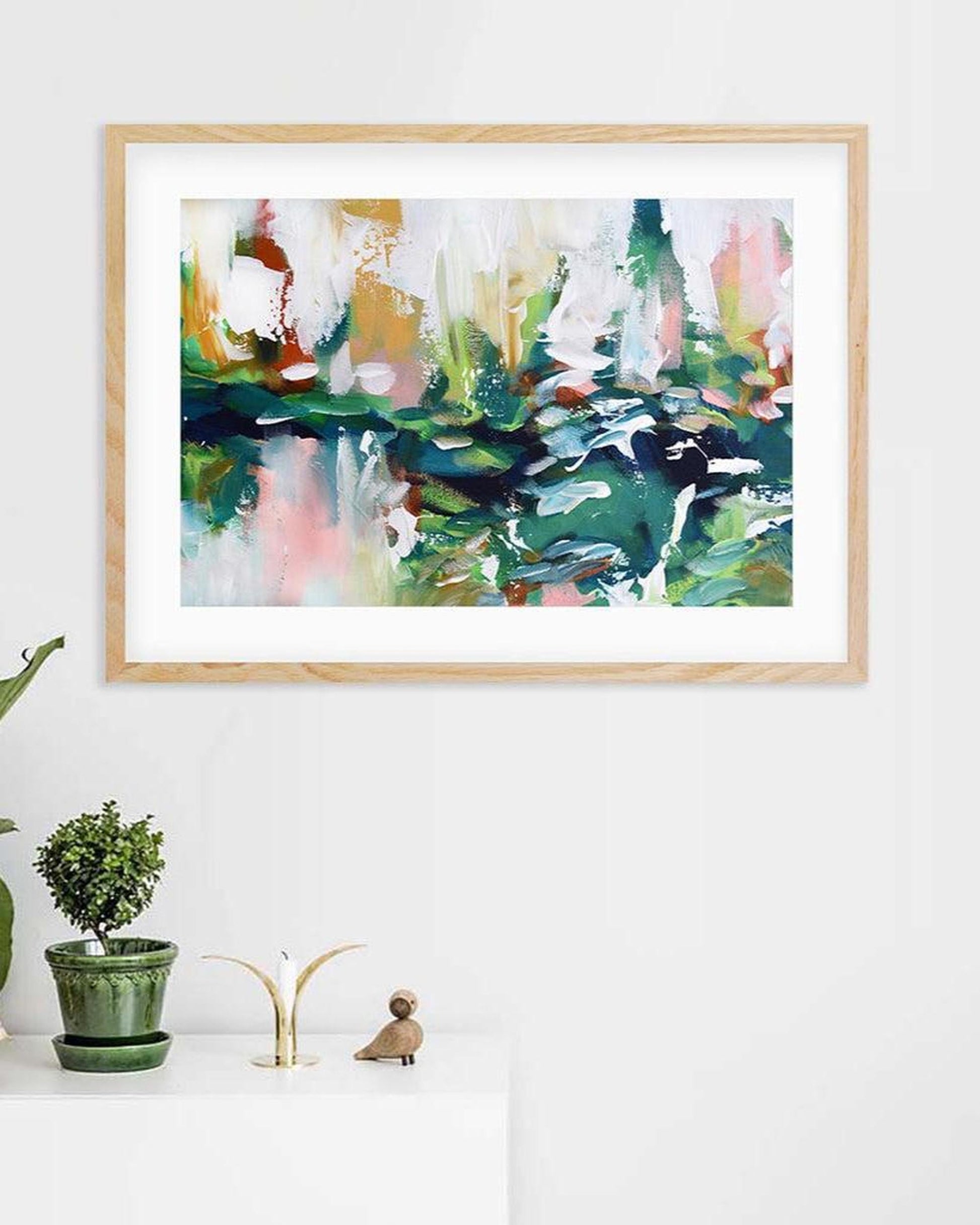 Framed abstract art print on a white wall with decorative items below.