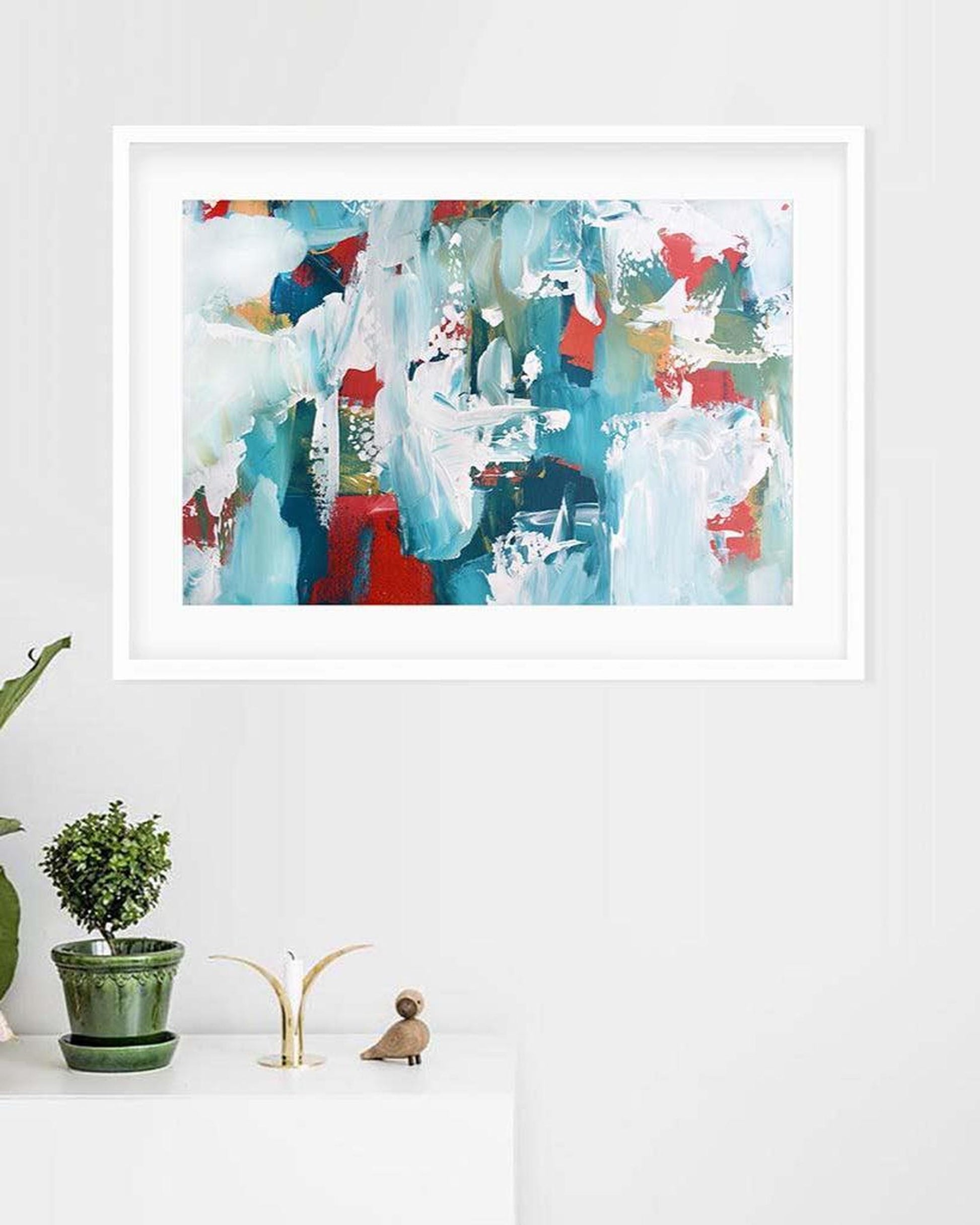 Framed abstract art print on a white wall with decorative items below.