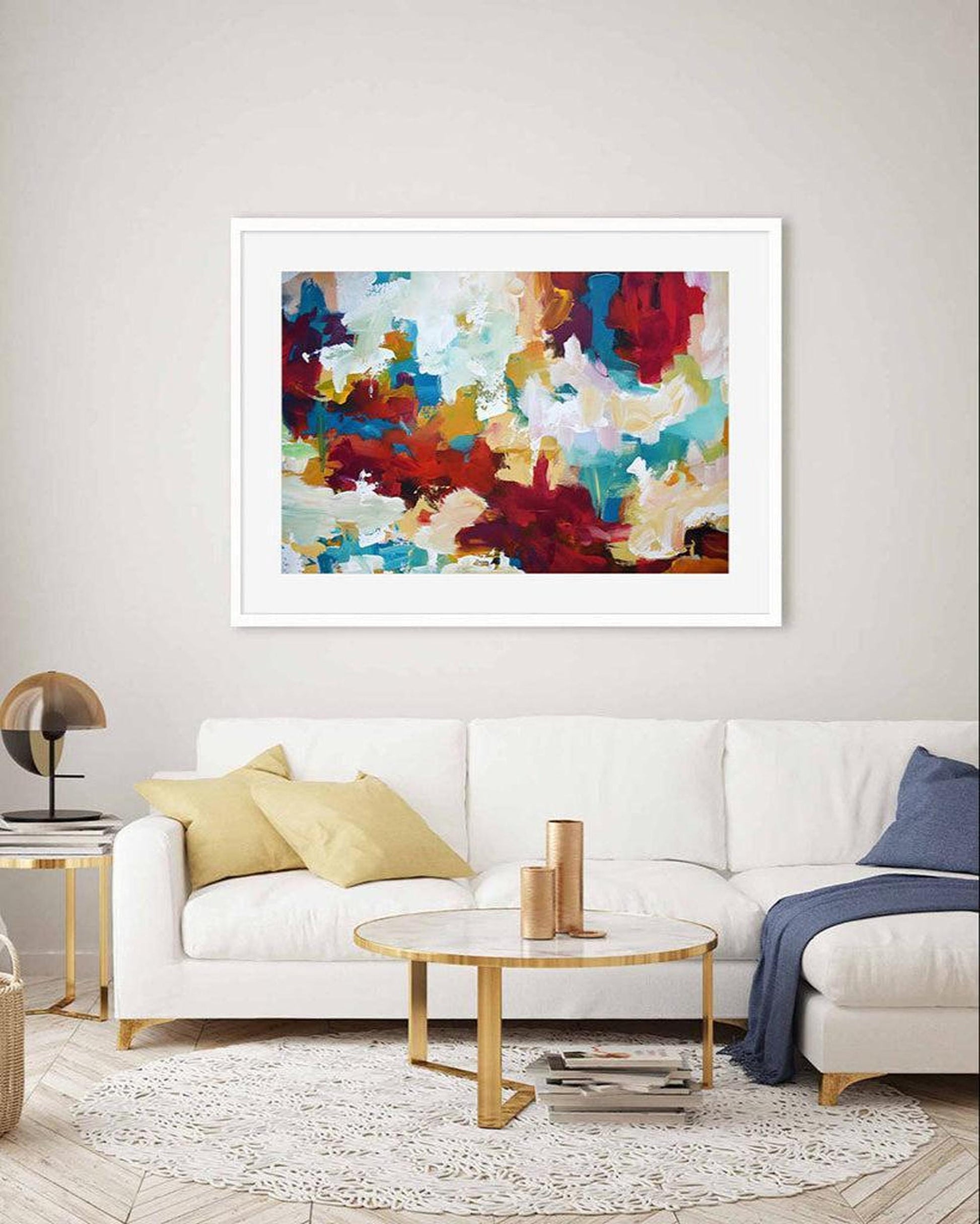 Colorful abstract painting in a white frame on a wall above a white sofa.