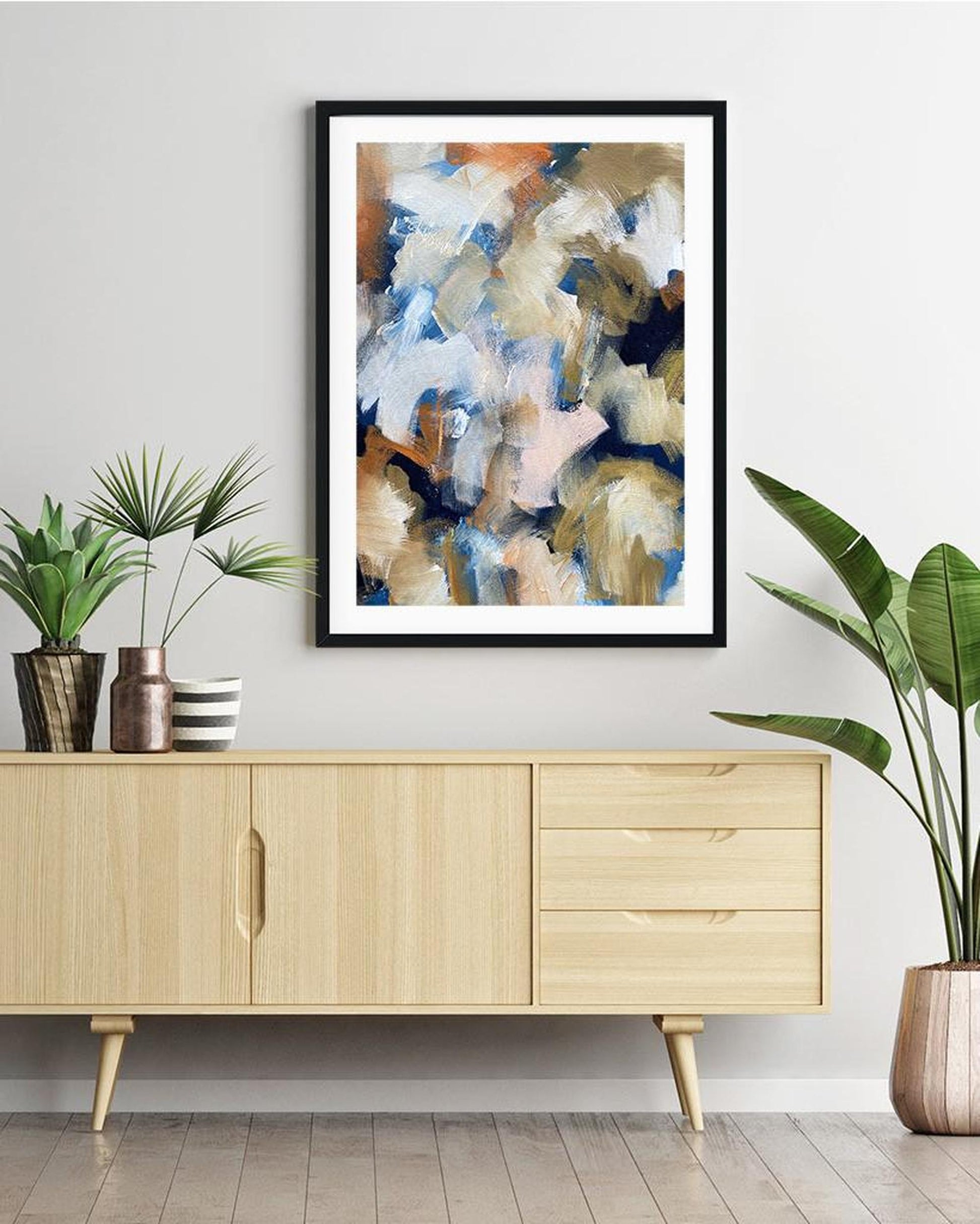 Abstract art print on a wall above a wooden cabinet with plants around.