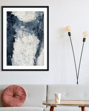 Abstract art print in a black frame on a wall above a sofa with a pink pillow.