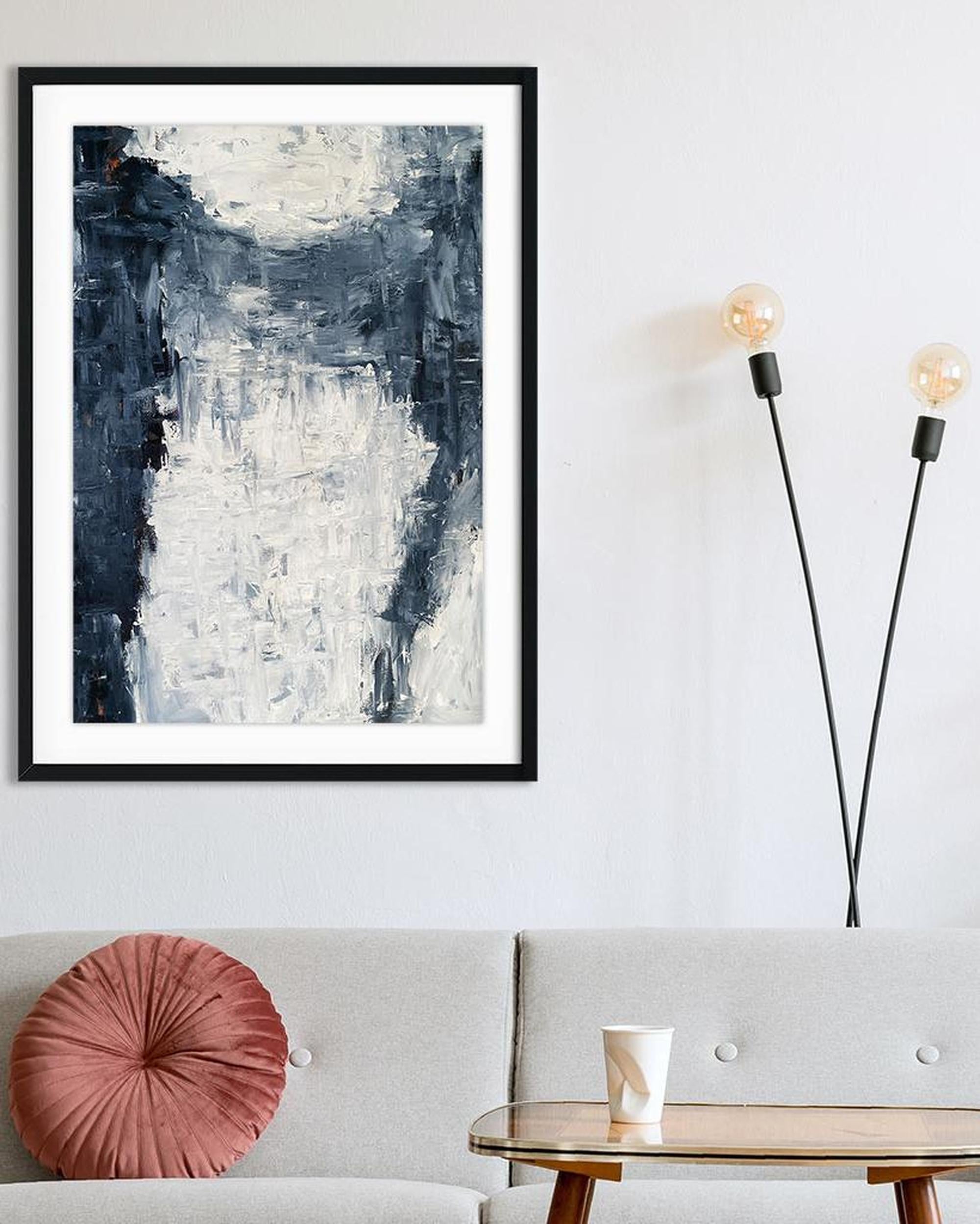 Abstract art print in a black frame on a wall above a sofa with a pink pillow.